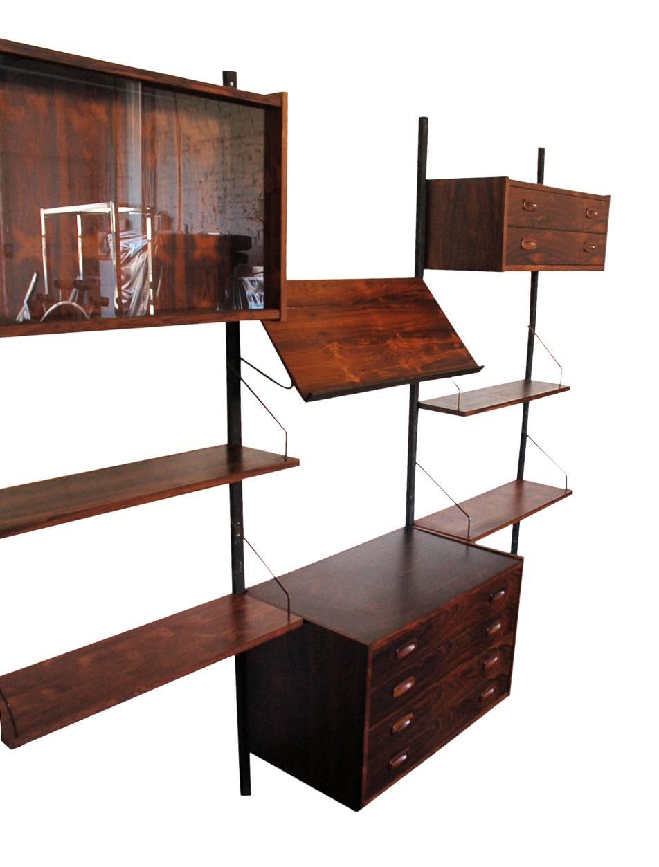 A three bay rosewood PS wall system designed by Peter Sorensen for Randers circa 1960's. It features 2 drawer cabinets, 1 glass display case, 1 magazine tray, and 4 shelves. All done in beautifully grained rosewood. Please note, the glass display