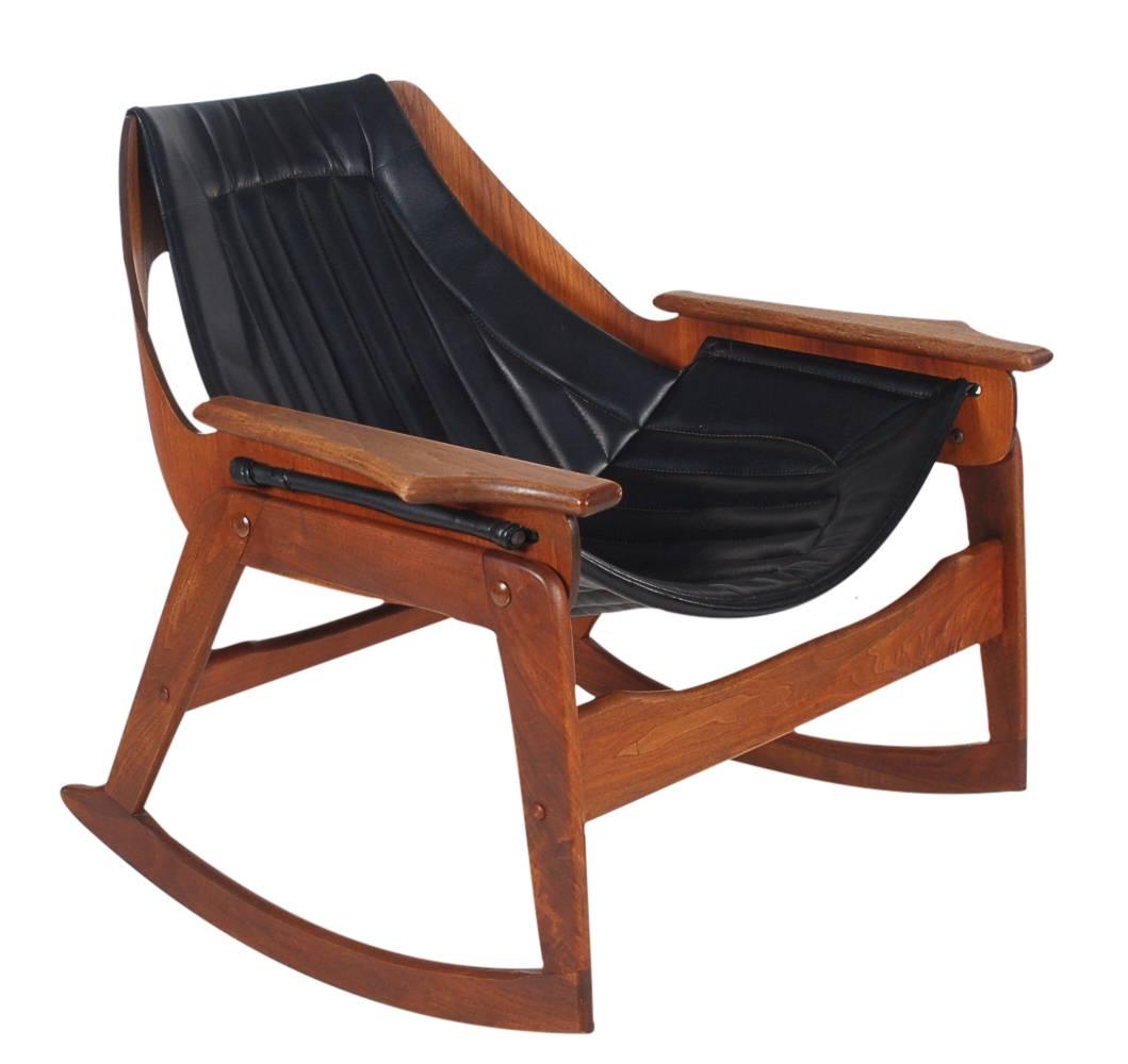 A very hard to find and cleverly designed rocking chair. It features a sculpted walnut frame with black Naugahyde sling upholstery. 

In the style of: Adrian Pearsall, Plycraft.