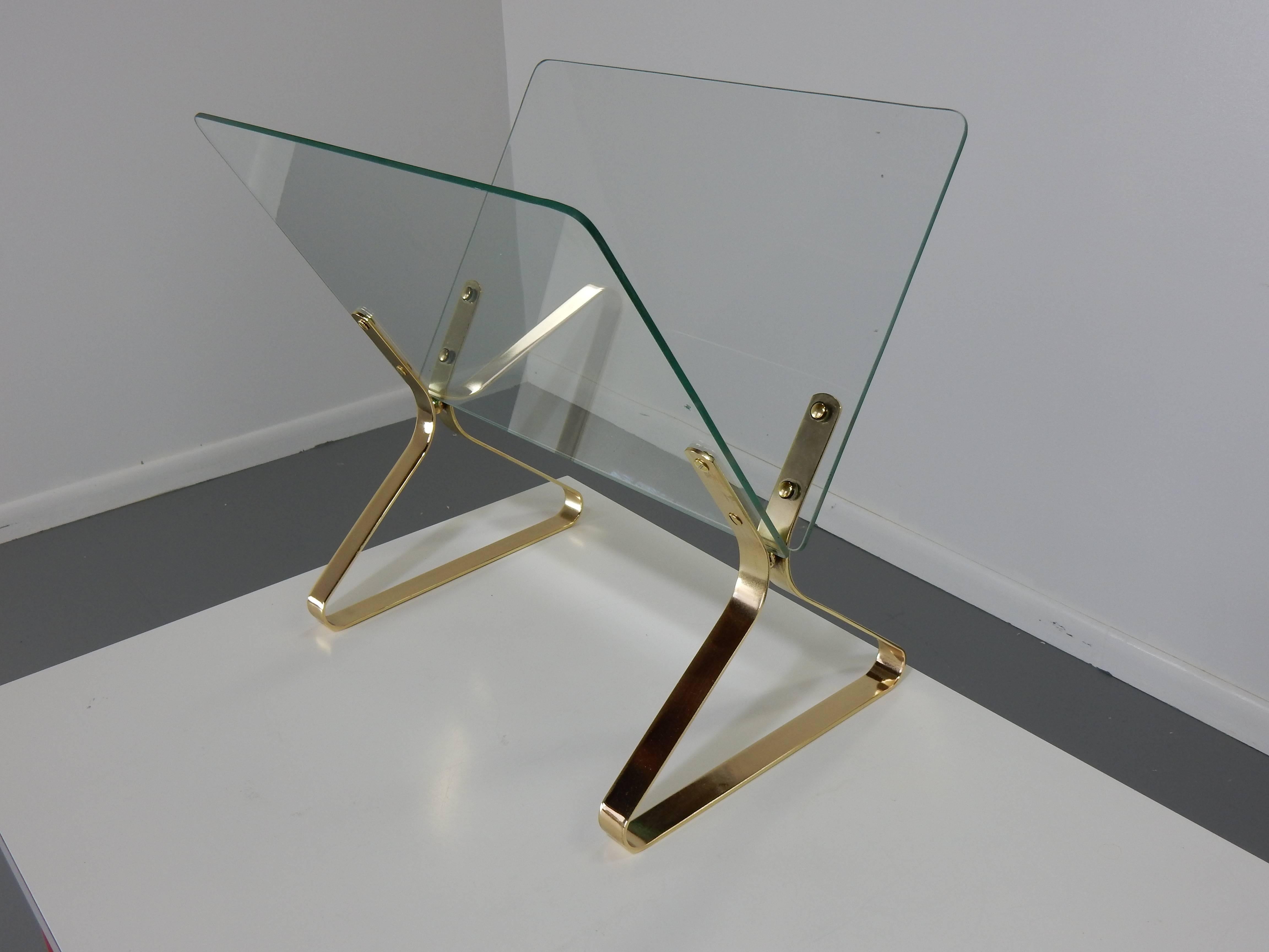 This is a glass and brass magazine rack by Milo Baughman. This rack will add a bit of luxury to any room.