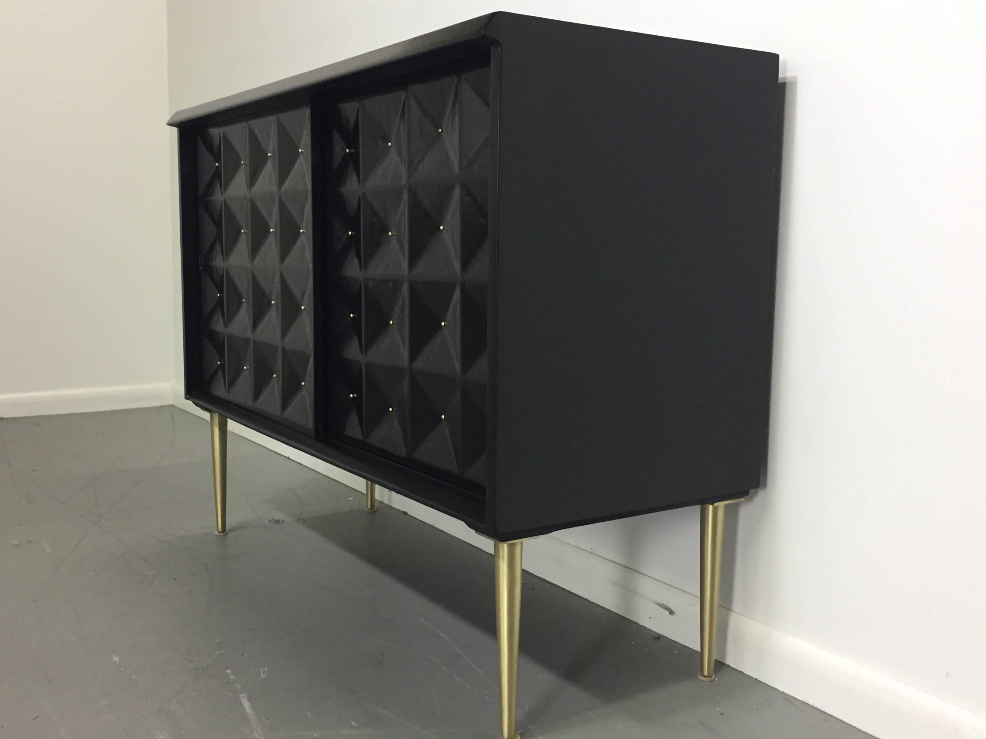 Petite sideboard with hand-carved inverted diamond shaped decorations with brass inserts on the two sliding front doors. This piece has two drawers on one side and one shelf on the other. The case has been ebonized and the legs have been