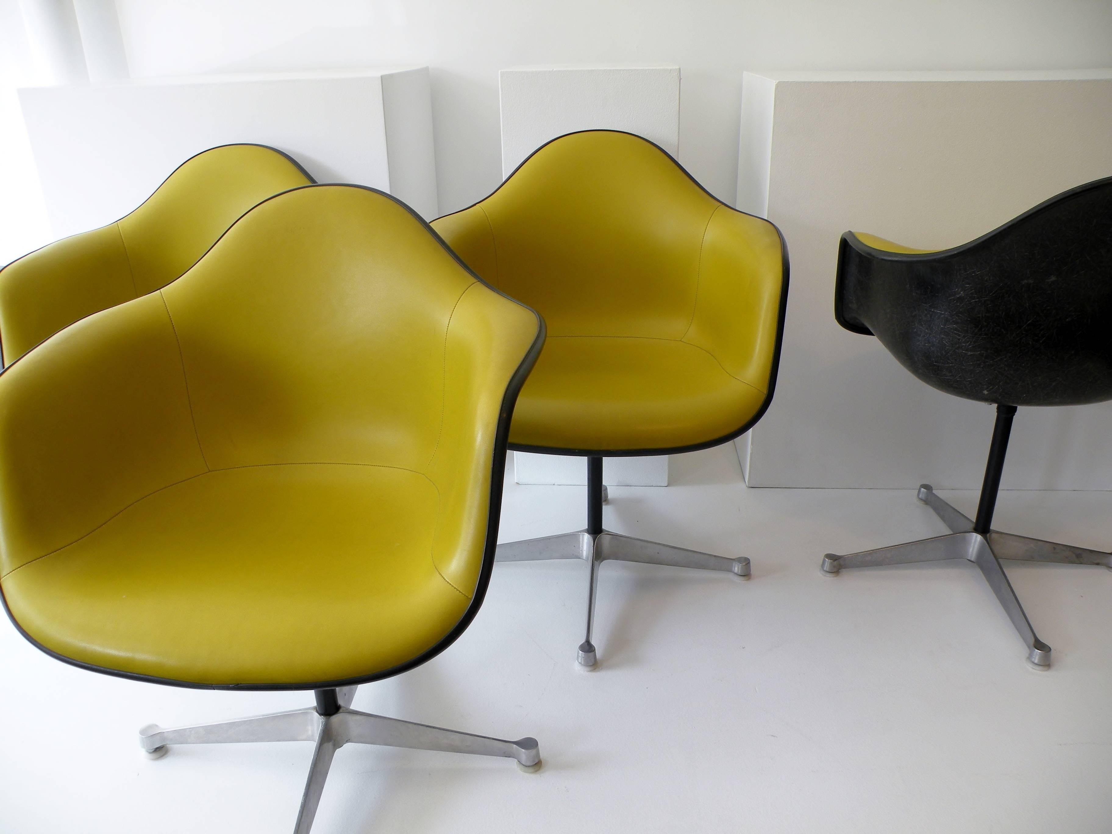 Set of four Aluminum Group armchairs black fiberglass shells showing pronounced fibers to surface, striking contrasting chartreuse vinyl seat covers, on four point bases. Designed by renowned Charles and Ray Eames for Herman Miller, these examples