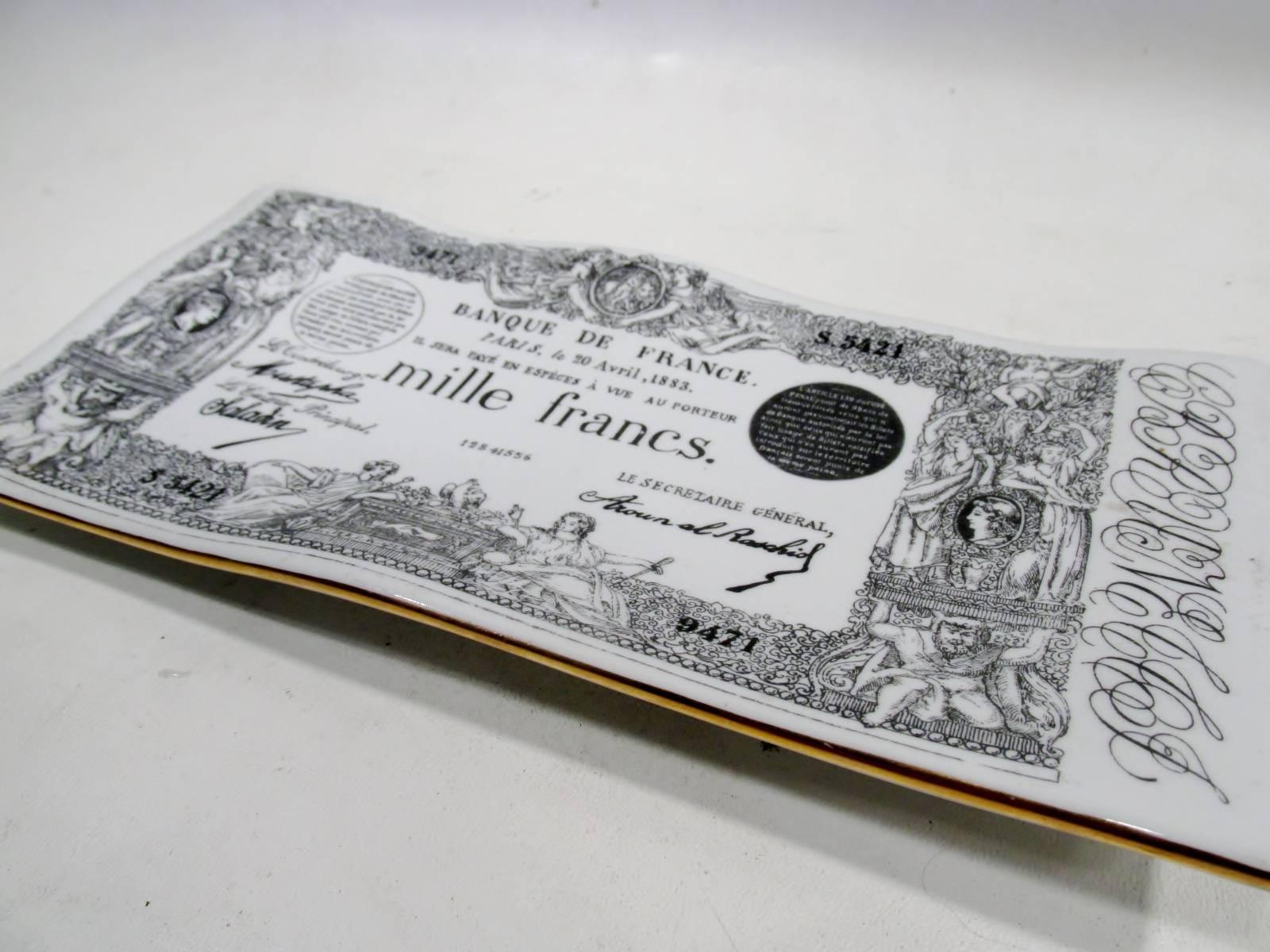 Early production Piero Fornasetti Italy “Mille Francs” ceramic vide poche tray. Approx. 9.75” long, 4.75” wide and 1” tall, mark dates to the 1950s with black printed decoration and gilt rim. Often time referred to as a desk pen tray, a “vide poche”