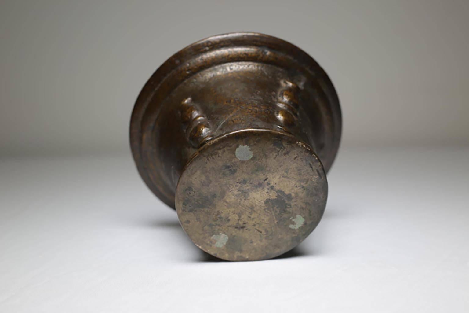 Bronze mortar that reflects a form common to the 16th century. The mortar was formed with a flared rim and slightly extended base. The body displays raised vertical, ridged bars, resembling half pilasters, surrounding the piece. It makes a great