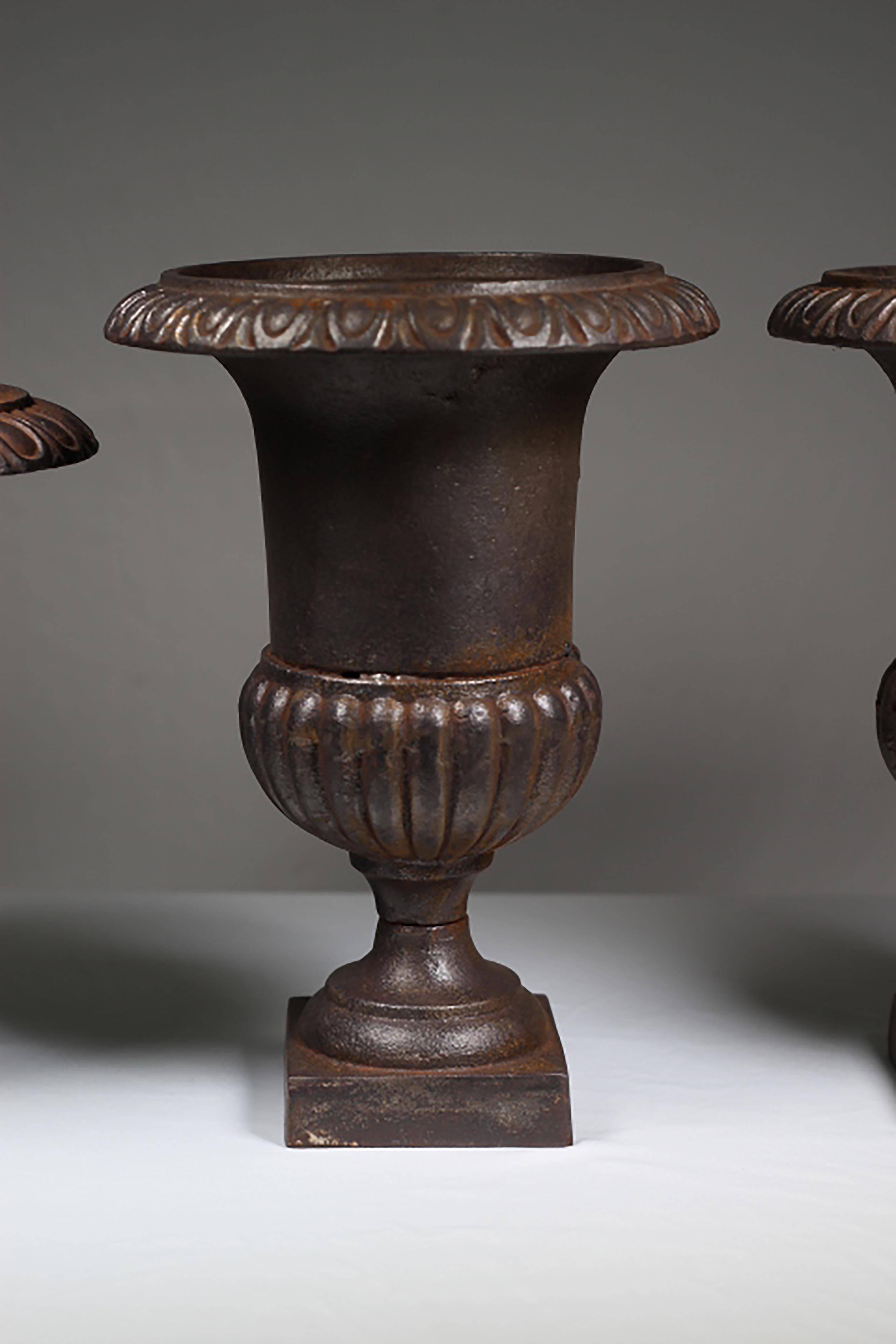 Vintage weathered cast iron urns on pedestal bases. Very substantial in weight. Good vintage condition with age appropriate patina.