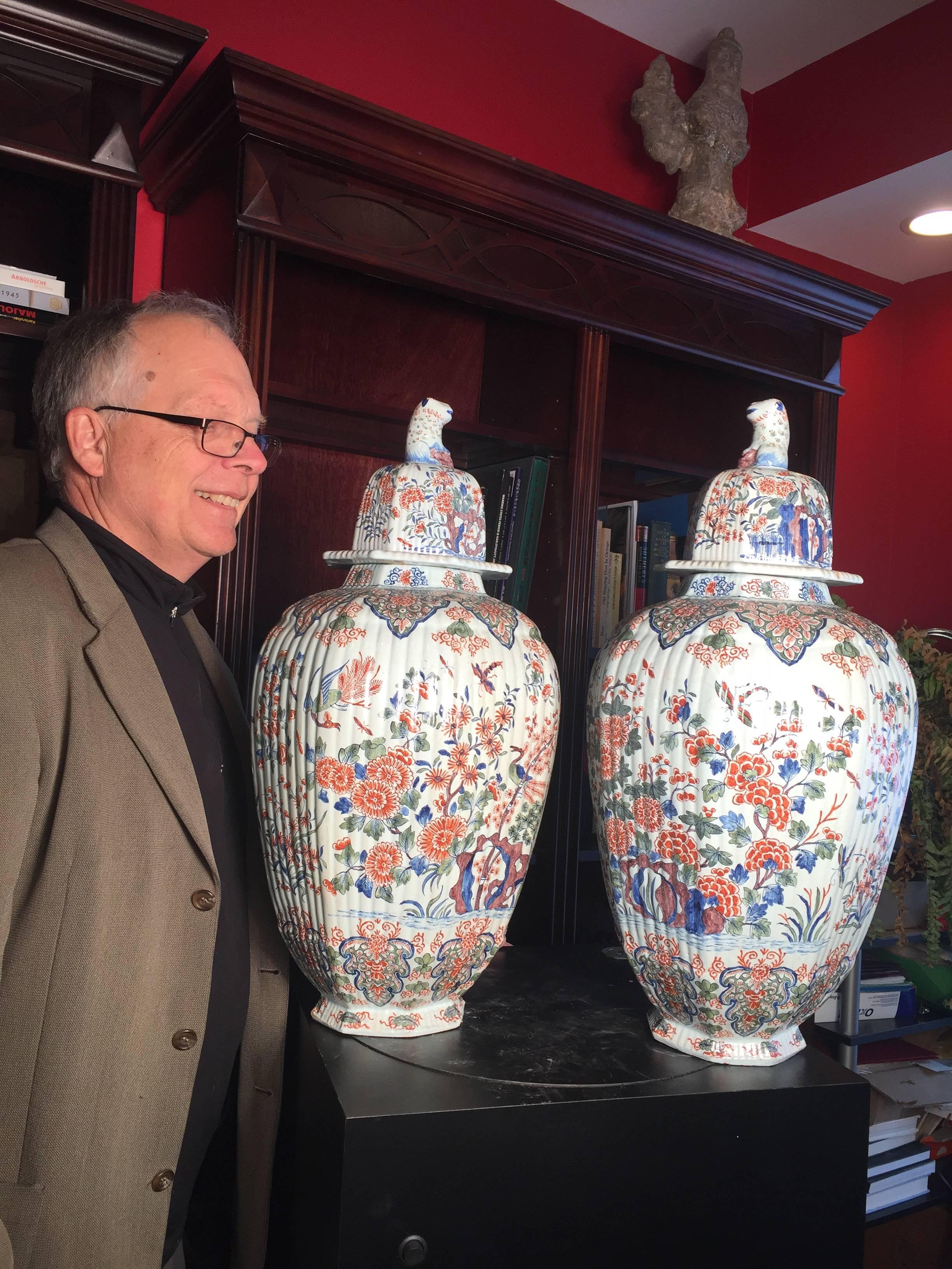 A, monumental 17th century pair of hand painted and hand glazed chinoiserie Imari birds and butterflies polychromed vases
-deckelvasen-  with lion finials, faceted and ribbed walls.

SIGNATURE: Signed bases: Delft House of Adrian Pijnacker, red