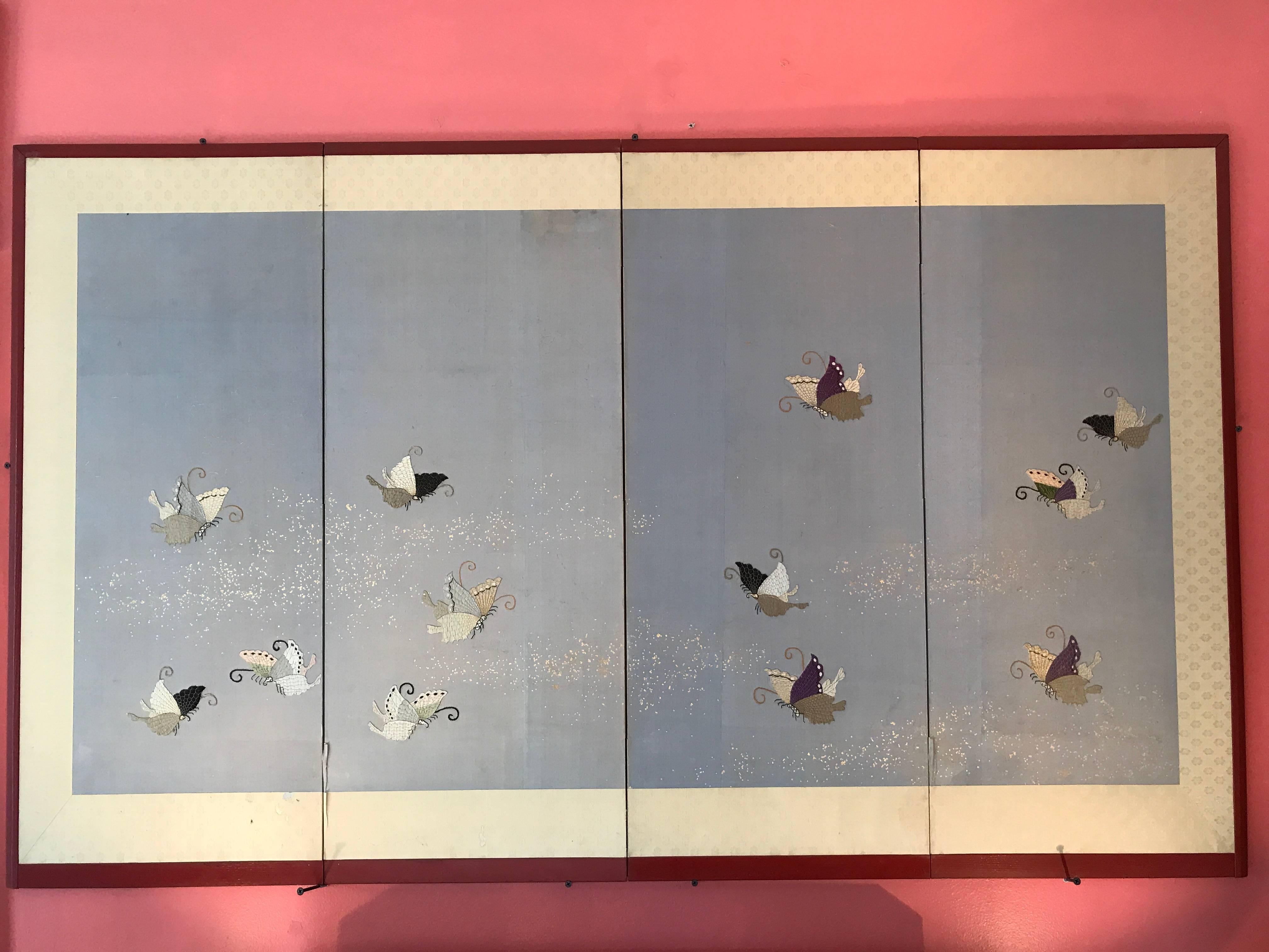 Japan, a beautiful and unusual four-panel screen Byobu with 12 hand embroidered Butterflies -Shushu- applied to its blue sky colored silk cloth surface and finished with a powdered gold mist in the back ground. It has been nicely framed in rich red