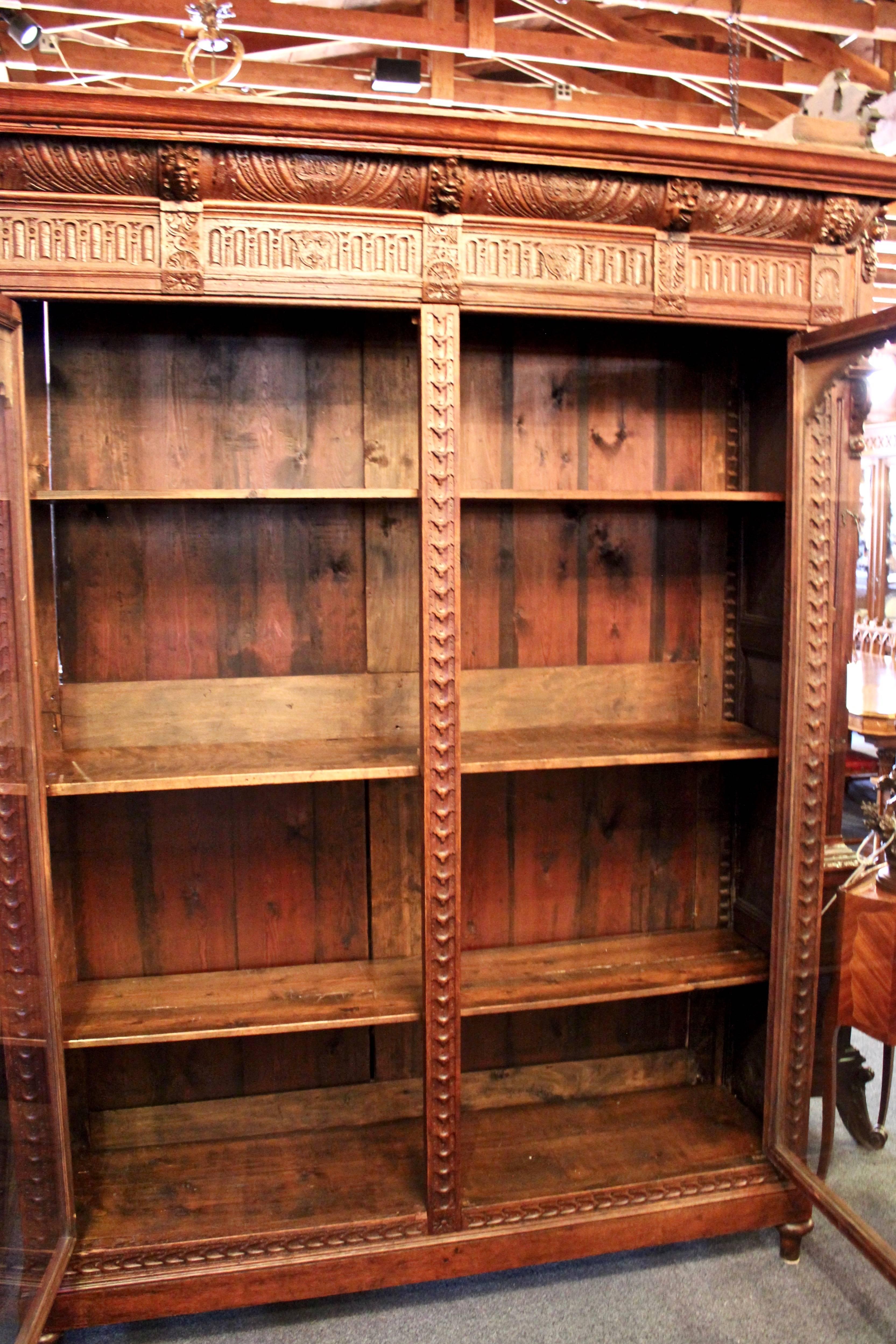 This hand-carved bookcase features two swing doors with glass fronts. Each of the nine faces that line the top are unique from the other. Two shields flank the center face with the text "Anno" on one and "1633" on the other.