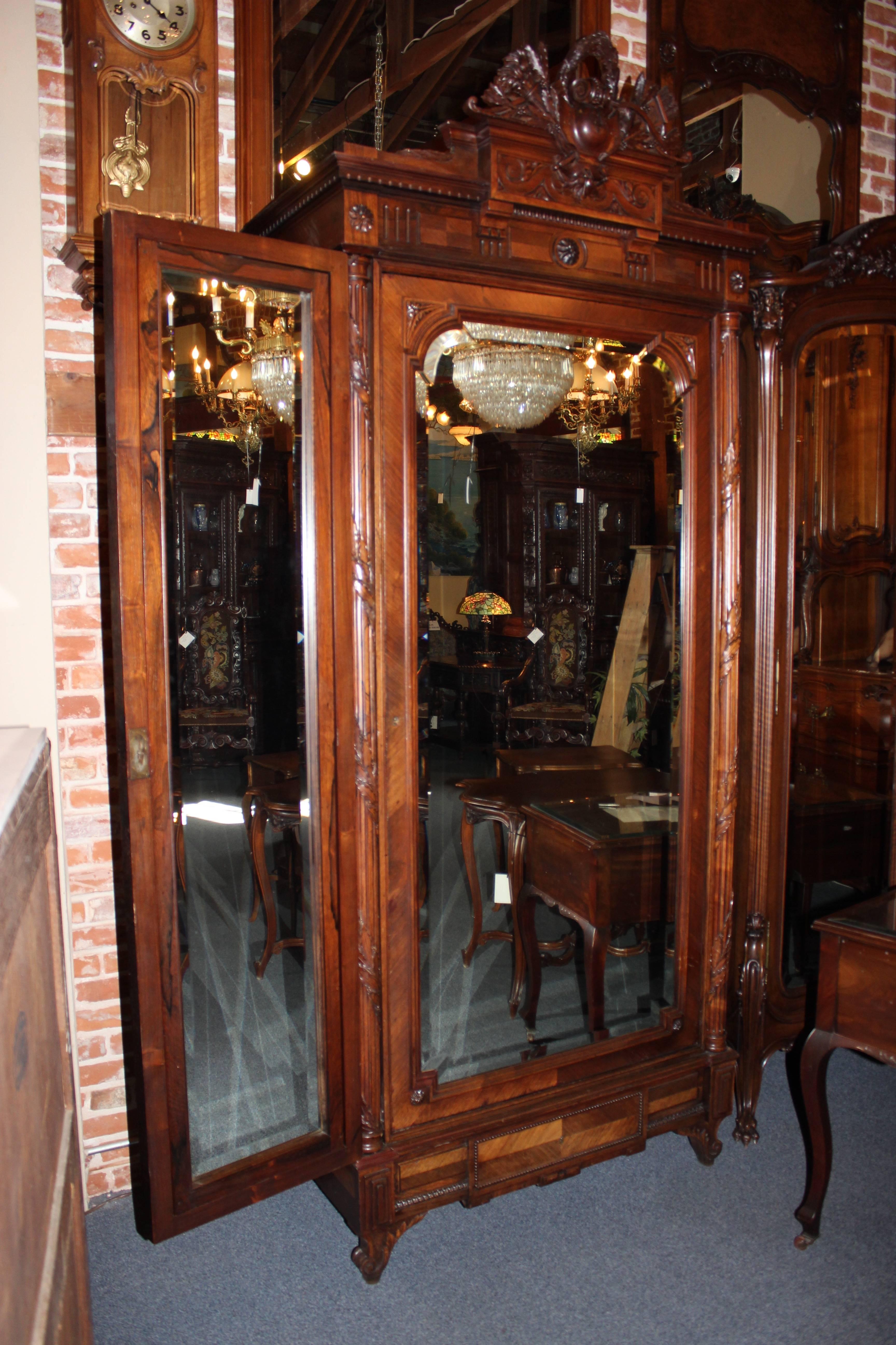 This 20th century French armoire is hand-carved from rosewood. The piece features two sides that can be extended and flipped to show either mirrors or the gorgeous wood. There is one pull-out drawers on the bottom while the mirrored front opens to