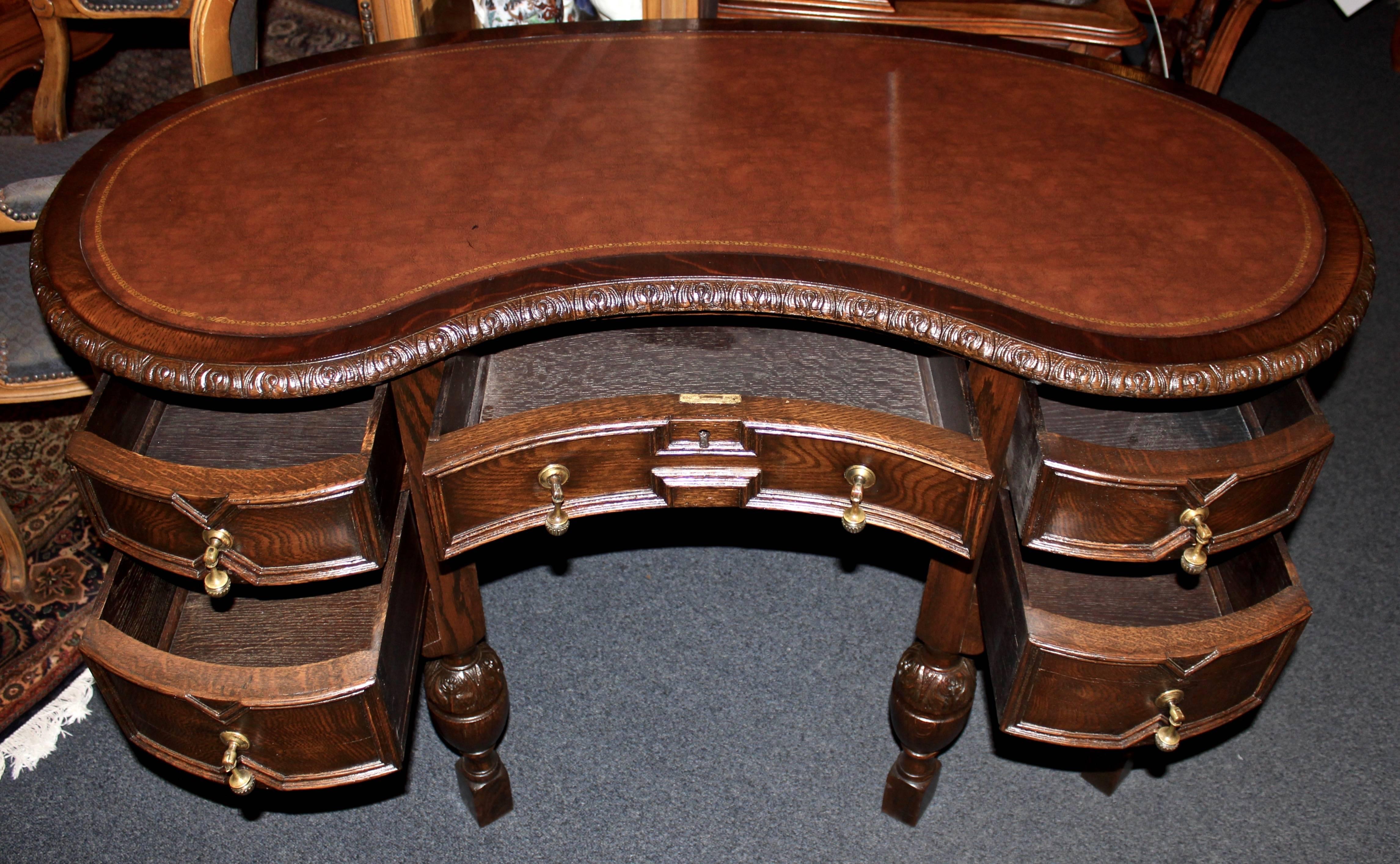 This English oak desk is made in a kidney shape in the straight-lined, Jacobean style.  It features carvings that are indicative of the minimalistic style as well as an embossed leather top.  Storage includes 5 pull-out drawers.  