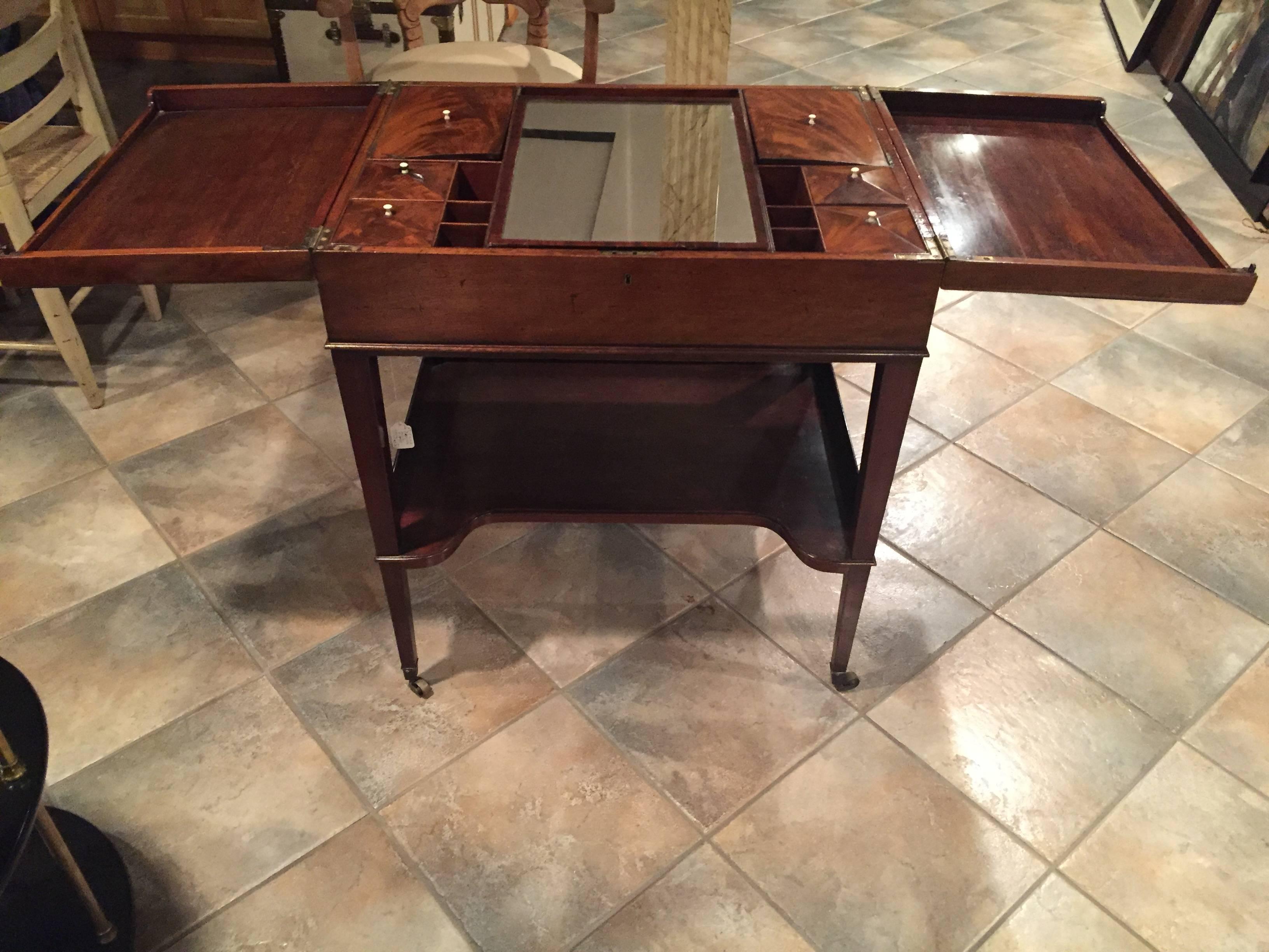 George III mahagony gentleman's dressing table. Two sides unfold to reveal cubbies with center easel action mirror. Lower shelf for additional storage. All upon original brass cassters.