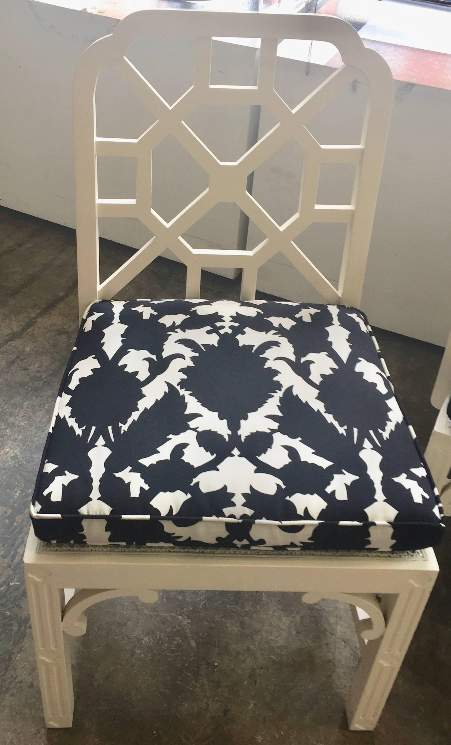 A set of four painted creamy white Chinese Chippendale style chairs comprising of two-arm and two side chairs having caned seats and new loose black and white cushions over fretwork on the front and sides of the legs.