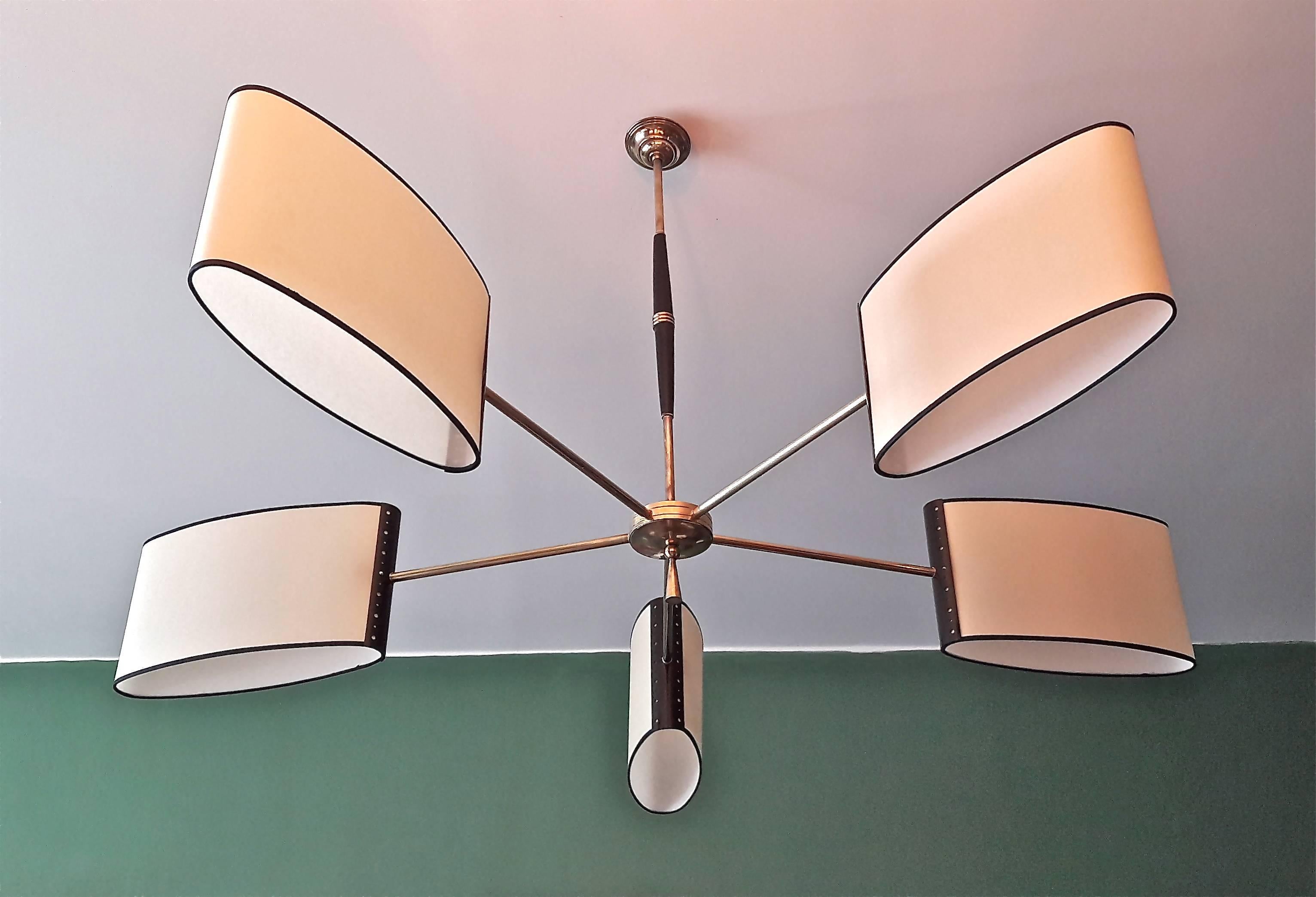 Brass and wood circular chandelier consisting of five lighted brass arms on which are arranged oval-shaped lampshades, fixed on perforated metal plates.
The arms are connected by a circular brass plate decorated with a brass pendant under the base.