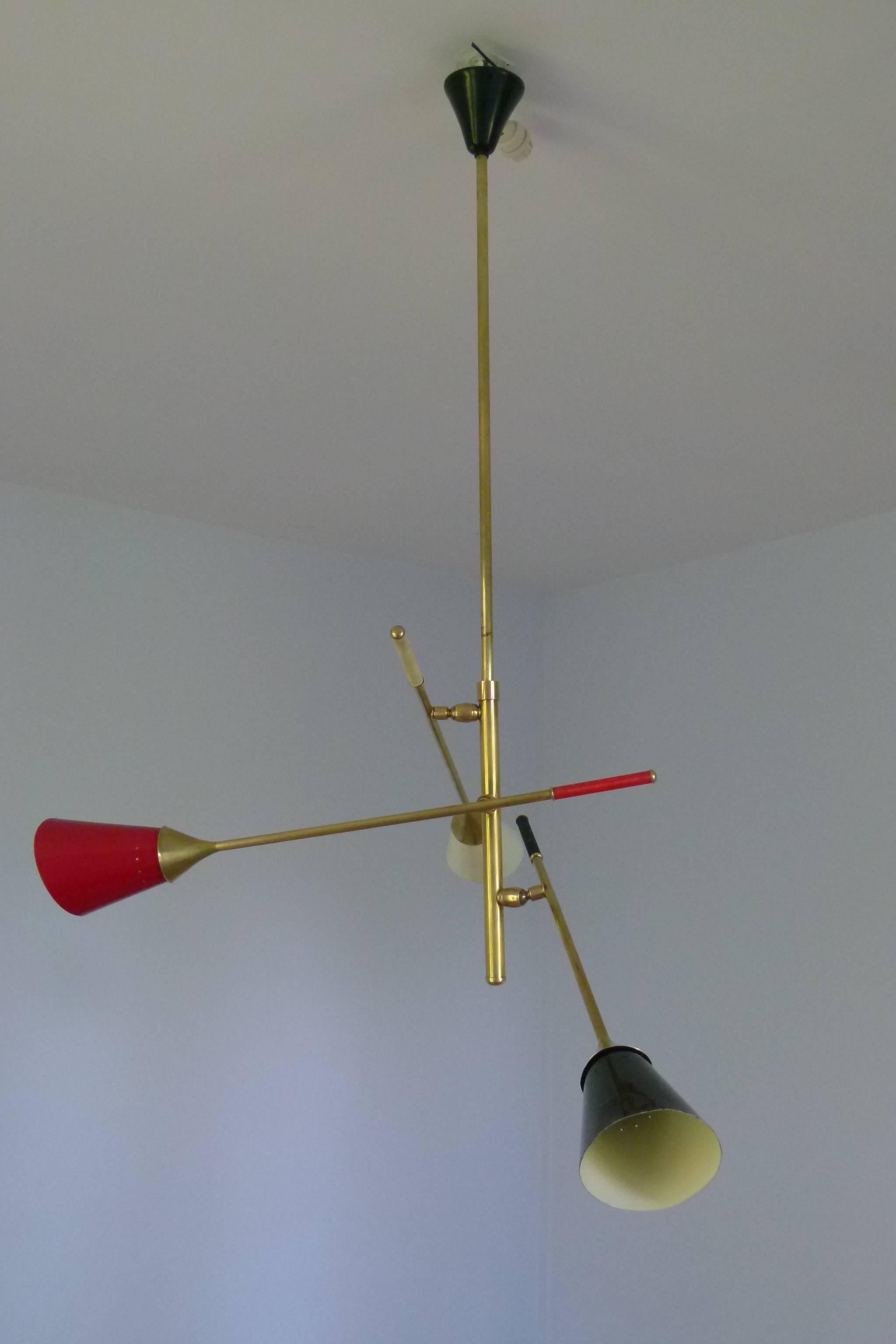 Brass and lacquered metal chandelier consisting of a main brass rod on which are set of three lighted arms mounted on patella for convenient orientation. Each arm is surmounted by a perforated colored metal lampshade and a matching color plastic