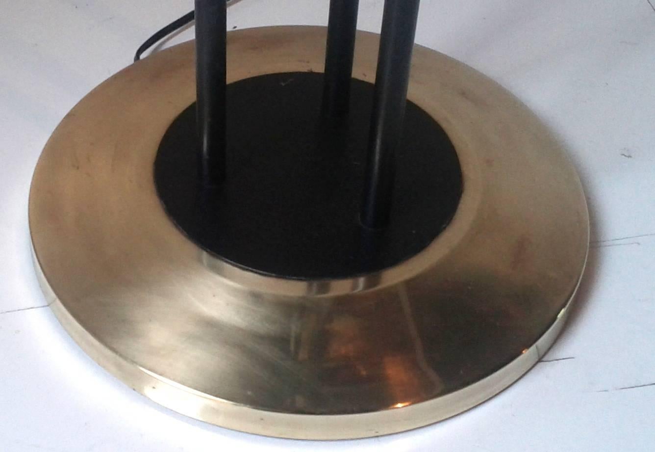 Floor lamp with three lights consisting of a circular brass base on which are set three lighted arms in black lacquered metal, surmounted by white frosted glass tubular light caches.
Lacquered metal rods arranged around the lights caches are