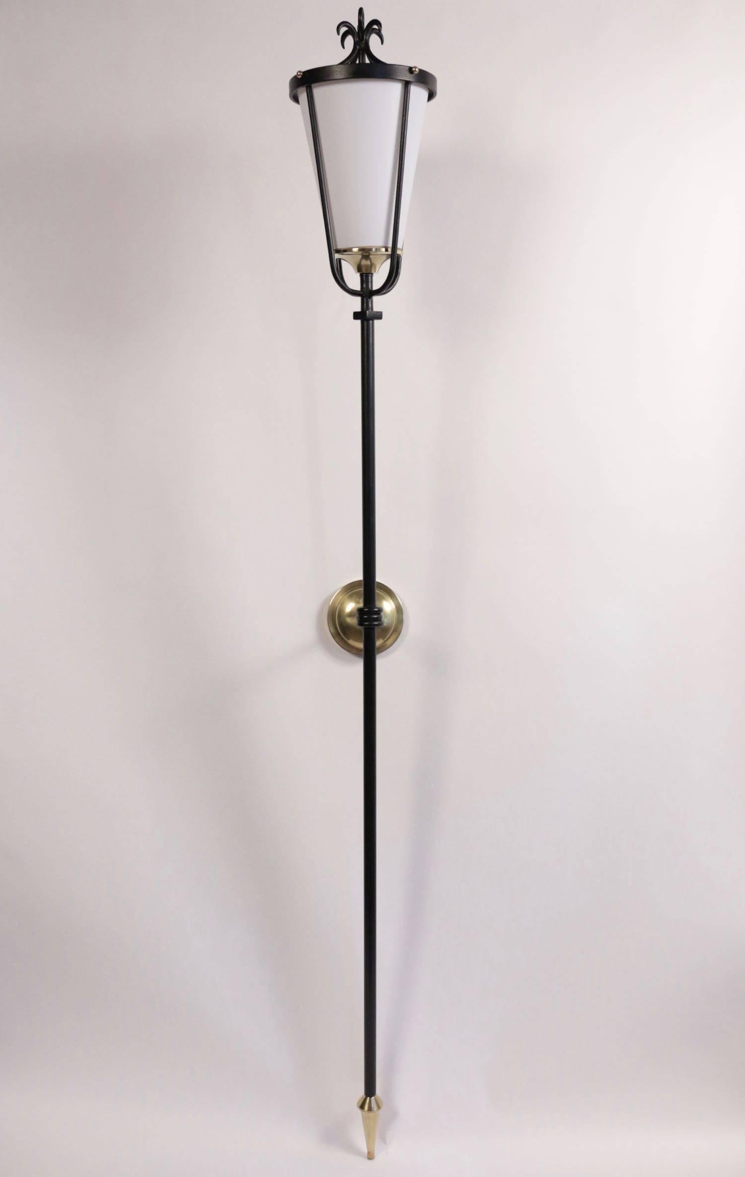 Pair of flare sconces in black lacquered metal.
Black lacquer metal trunk on which stands a lantern with a lampshade. The trunk ends with a decorative pike. A support allows wall mounting. A brass cache hides the support.
1950s-1955s French work