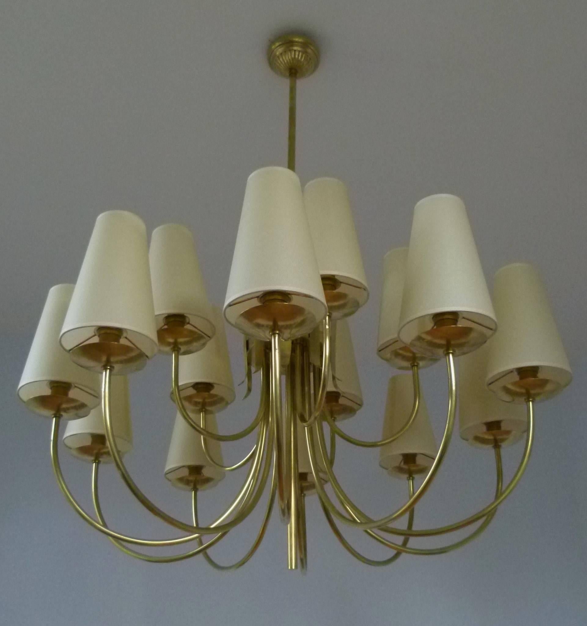 Large brass chandeliers composed of fifteen curved lighted arms. The arms are arranged in two rows. Ten at the bottom and five at the top and are terminated by brass discs supporting conical lampshades.
The lighted arms are fixed on a cylindrical