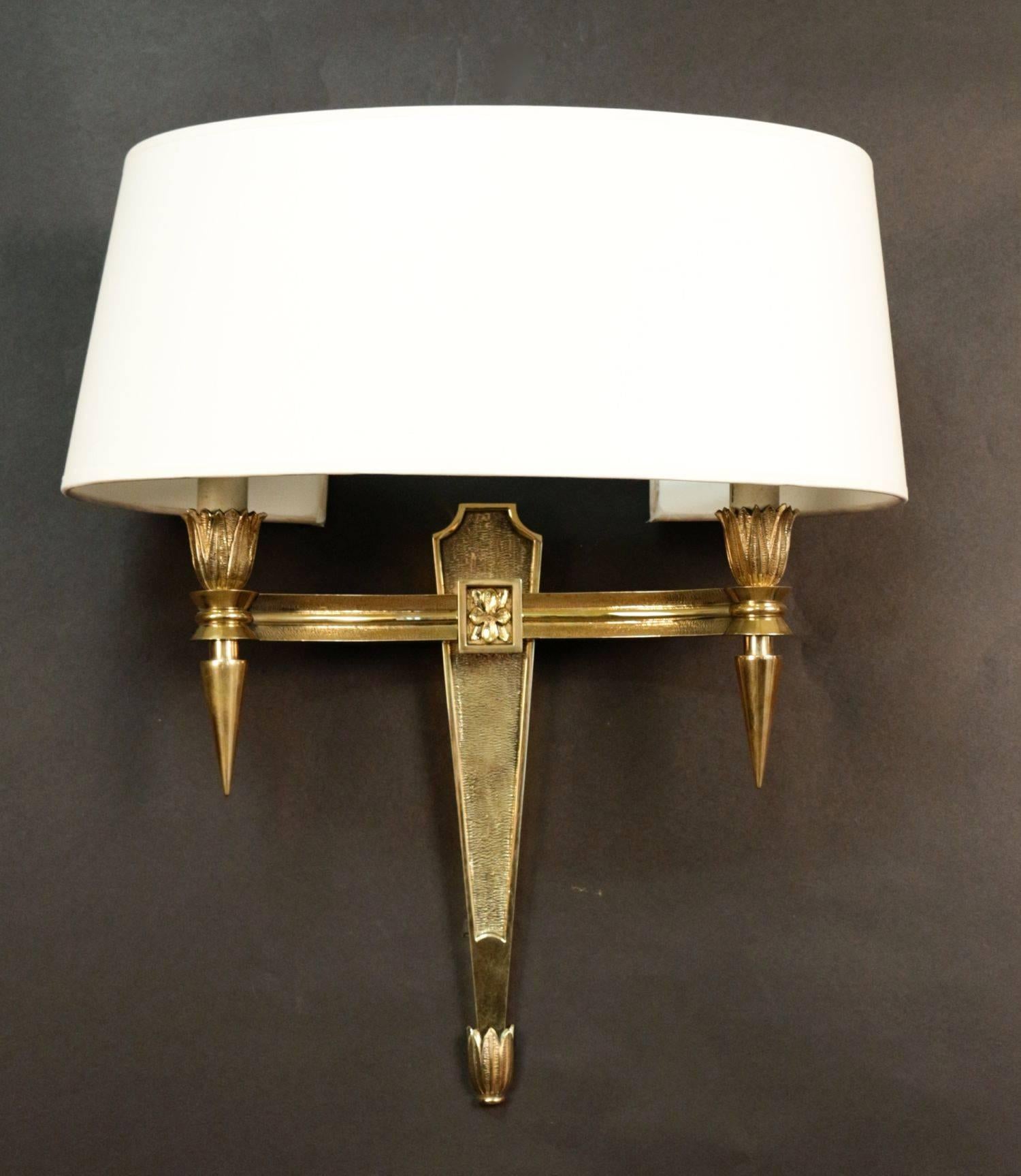 Pair of 1950s neoclassical sconces in chiseled bronze. They consist of two lighted arms with sockets endings supporting bulbs. French work. Probably by Maison Jansen. New lampshade redone according to the original. Perfect condition.