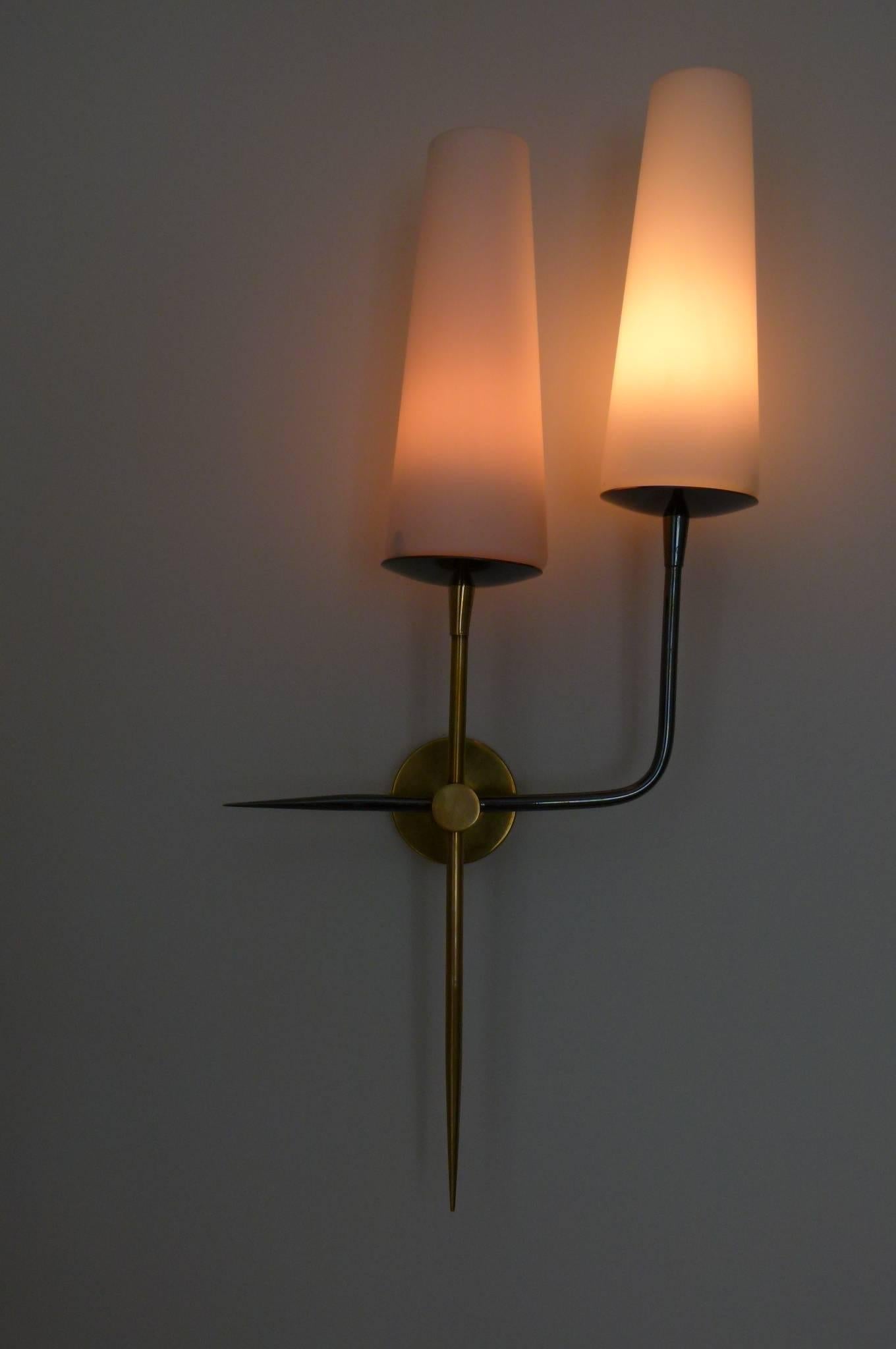 Pair of two sconces with two lighted arms consisting of a circular base on which are set two lighted arms. On straight brass arm with a white opaline lampshade and one right angle gunmetal finish brass arm also with a white opaline lampshade. Both