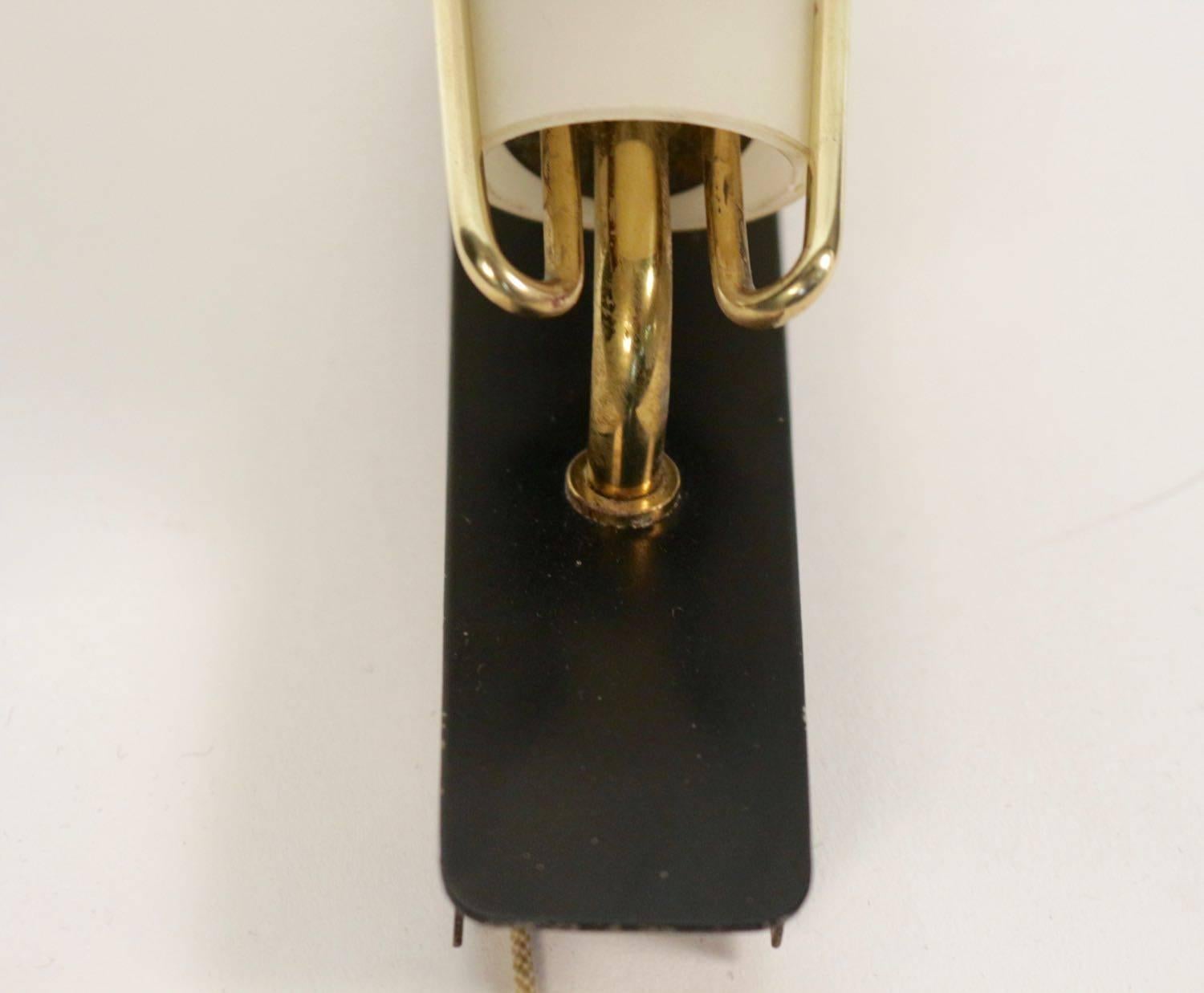 Pair of 1960s Italian sconces by Stillovo.
A black lacquered metal plate serves as a support for two brass rods in which fits a white conical shape opalin glass lampshade.
On each sconce a small cord allows to switch the light on and off.
1960s
