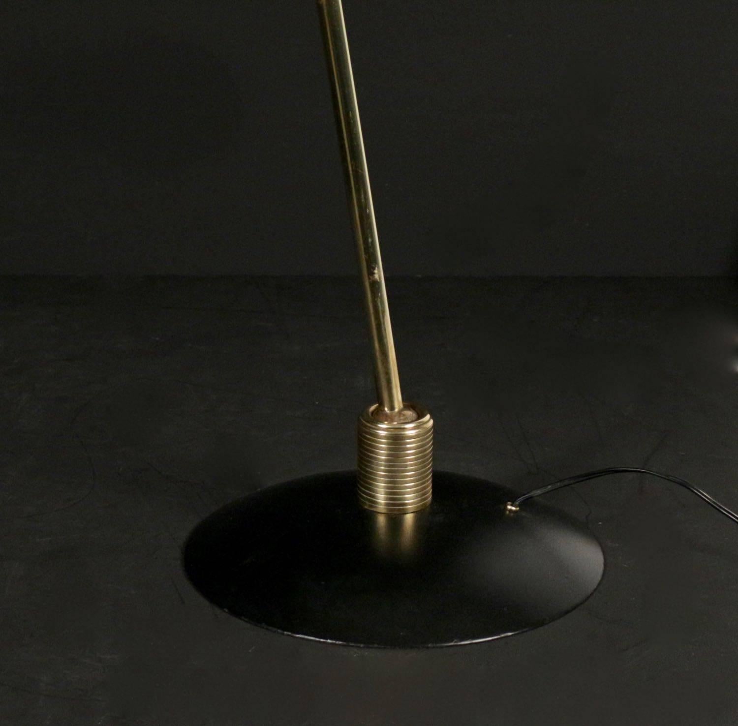 Brass and lacquered metal floor lamp. Consisting of a circular black lacquered base surmounted by an adjustable ball geared articulated foot and a double lampshade. The food ends with a double lampshade attached to a brass support equipped with two