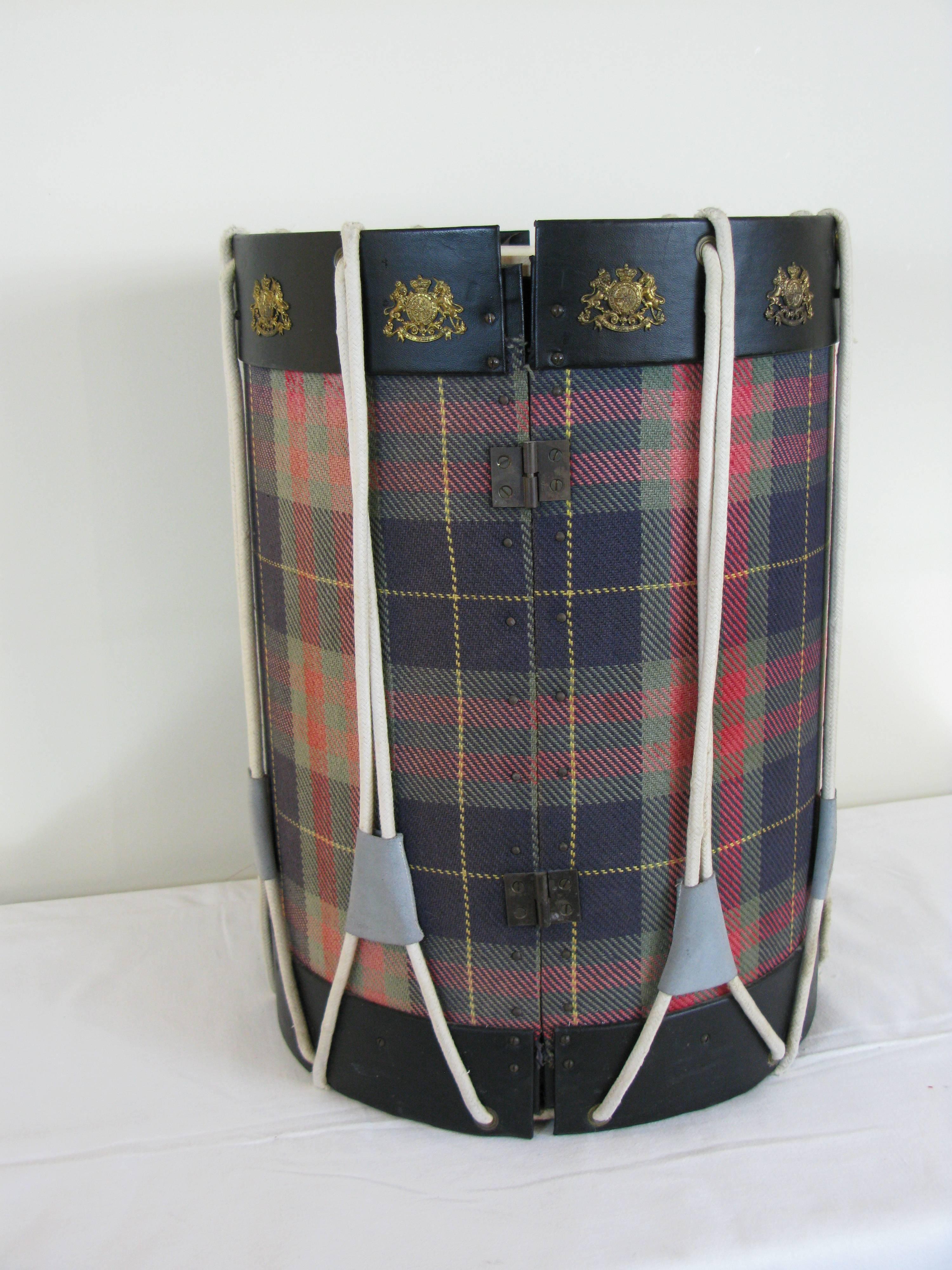 Bar unit in the shape of a drum covered with plaid fabric and black imitation leather wrapped around the edge and off white on the top.
Small cords depart from top to bottom of the cabinet.
Brass patterns are arranged on the bar top.
Two double