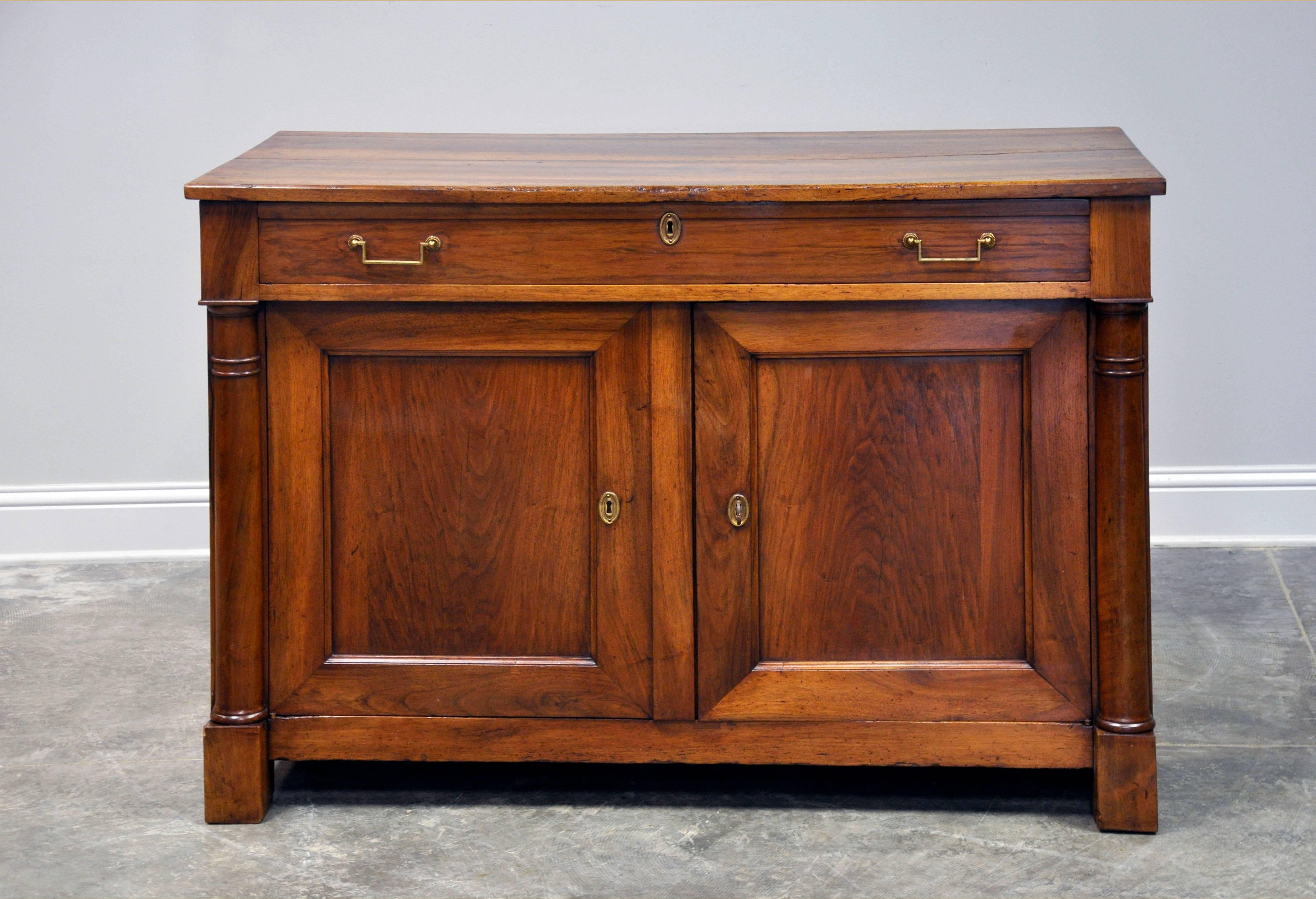 19th century French Empire style buffet in beautiful walnut lends the classic stylings of this case piece both warmth and depth. Carved wood pilasters frame a single drawer set above two cabinet doors complete with original brass escutcheons and