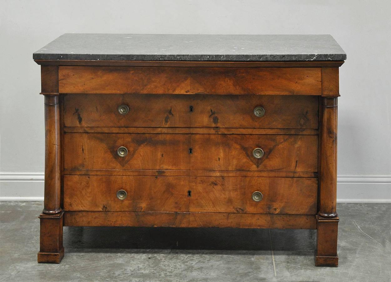 French Empire commode in beautiful burled walnut, original gray marble top and brass fittings. Solid wood columns frame four drawers, circa 1840. 

Established in 1979, Joyce Horn Antiques, ltd. continues its 38 year tradition of being a family