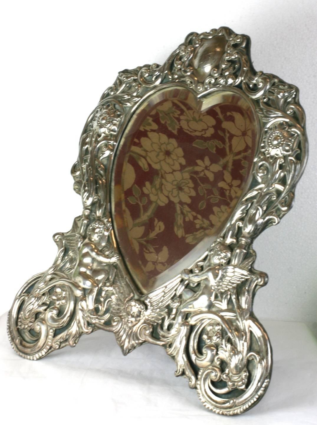 Elaborate and wonderful Victorian heart formed sterling dressing/vanity mirror, late 19th century English. Wonderfully high styled Victorian motifs with cherubs, sunflowers and elaborate scrollwork. The repousse sterling motif is backed on a velvet