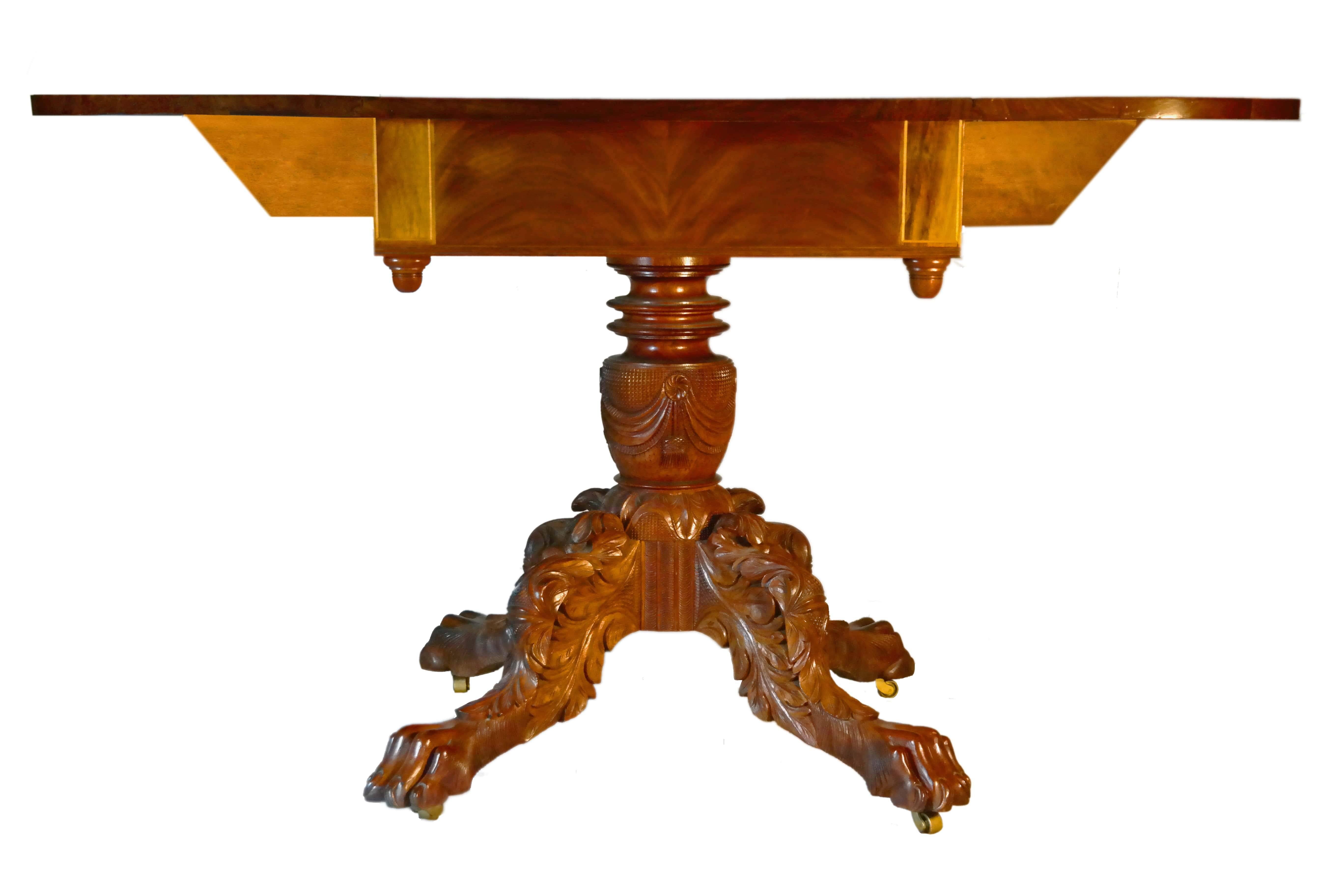 Late 19th century American mahogany Pembroke table. Top made of single solid boards with figured mahogany leaves. Satinwood stringing inlaid into mahogany skirt with an elaborately carved pedestal base resting on lion feet with original brass