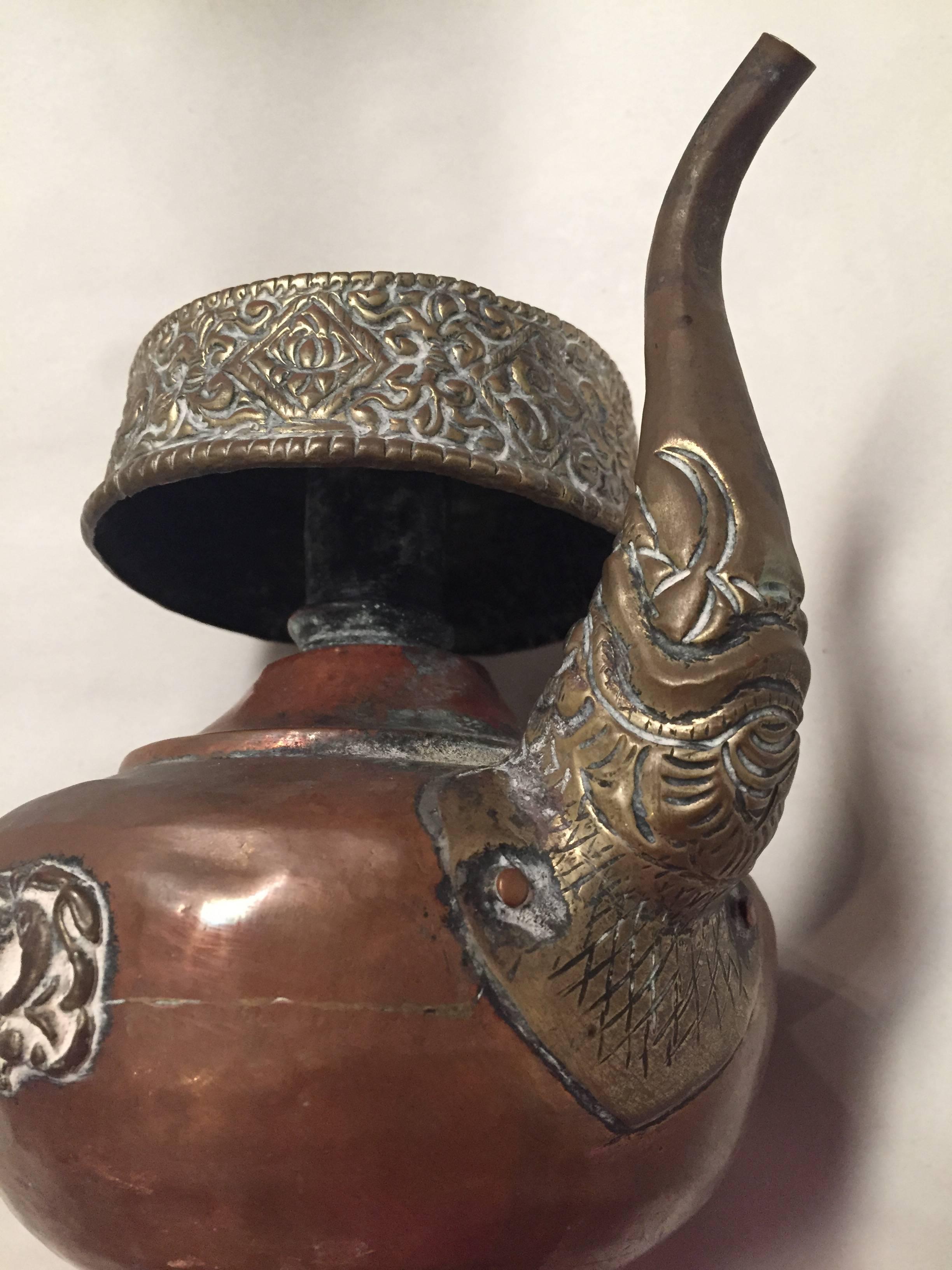 This beautiful Tibetan teapot is used to store and serve buttermilk tea. The pot is decorated with Tibetan auspicious symbols. The top is fully adorned with embossing of lucky signs and a lotus pattern. The elaboration extends to the spout of the