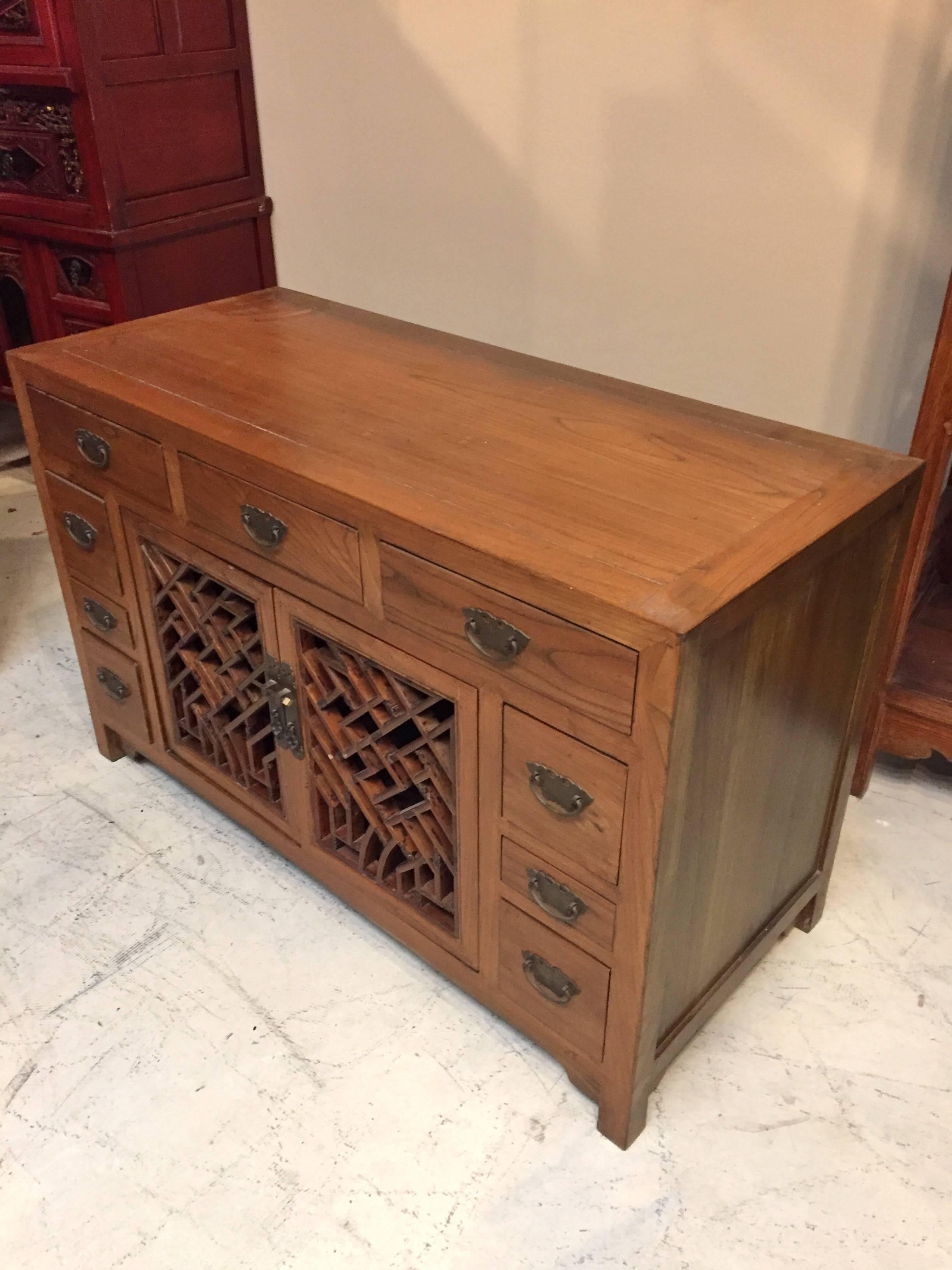 Substantial, solid wood Chinese chest with antique lattice work has nine full-length drawers. The wood is elmwood. It's prized for its beautiful, mountain like grains. Clear finish displays the color and patterns well. Butterfly shaped bronze