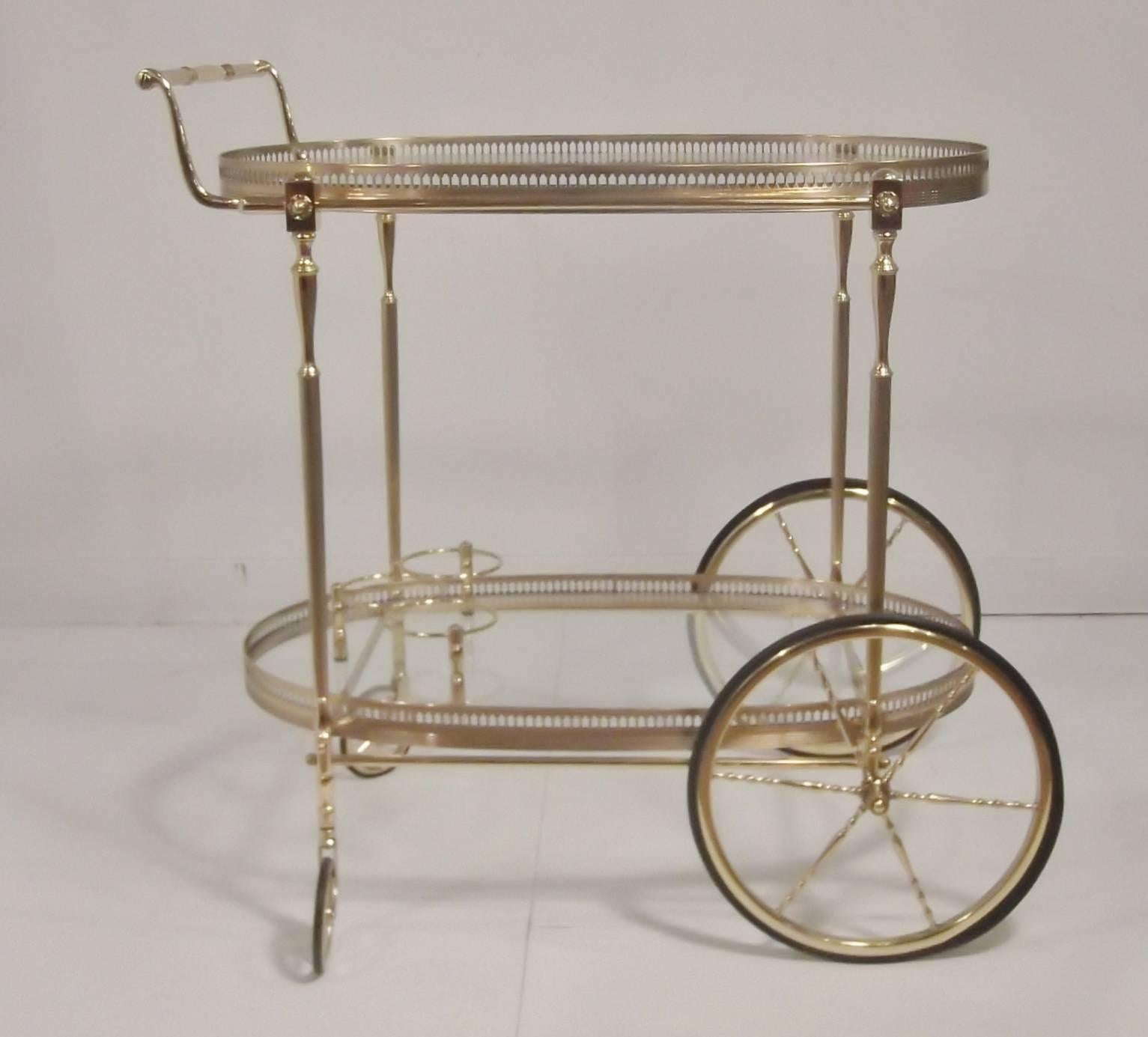 Oval polished brass two-tiered bar cart with gallery edge. The cart rests on two large and two small bicycle wheels with the front rotating 360 degrees.

The finish is bright and clean. The rubber on the wheels is fresh and pliable.