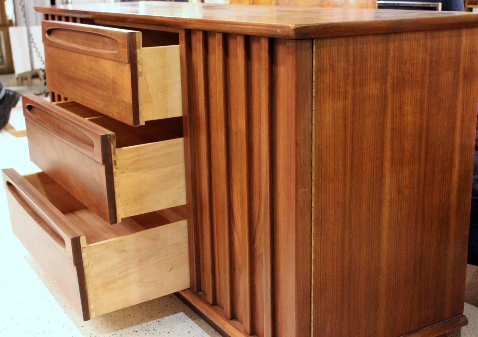 American of Martinsville Mid-Century walnut credenza.  Three centered drawers flanked by slatted doors revealing one fixed shelf on each side. The drawer handles are very tailored and recessed to give a clean live to the drawers. Fine American made