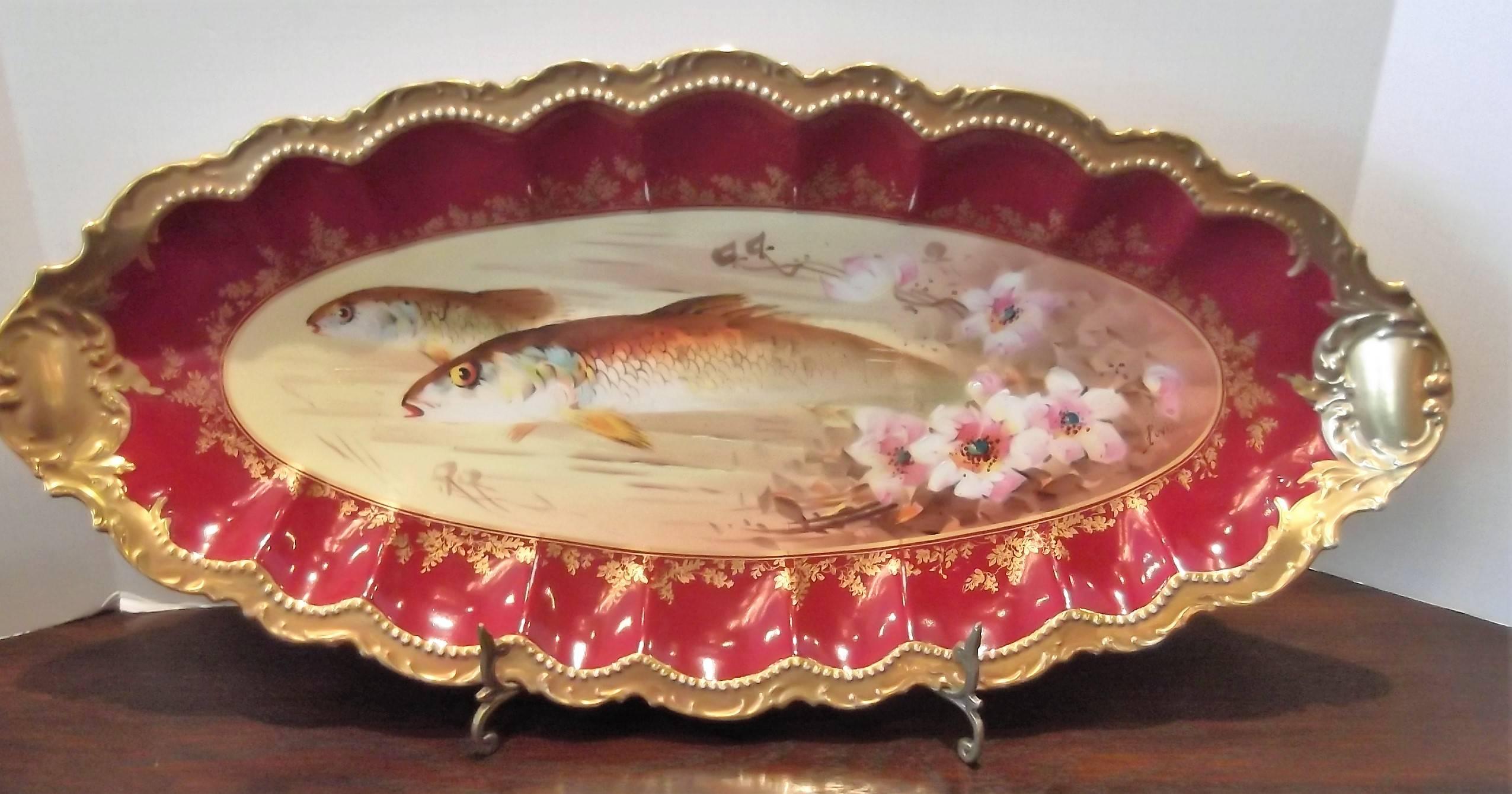 A set of 12 plates and one large fish platter, hand-painted with rich gilt border. The deep raspberry borders have a gilt leafy overlay. Measures: The plates are 9.5" diameter, the platter measures 11.25" high, 24.25" wide. The
