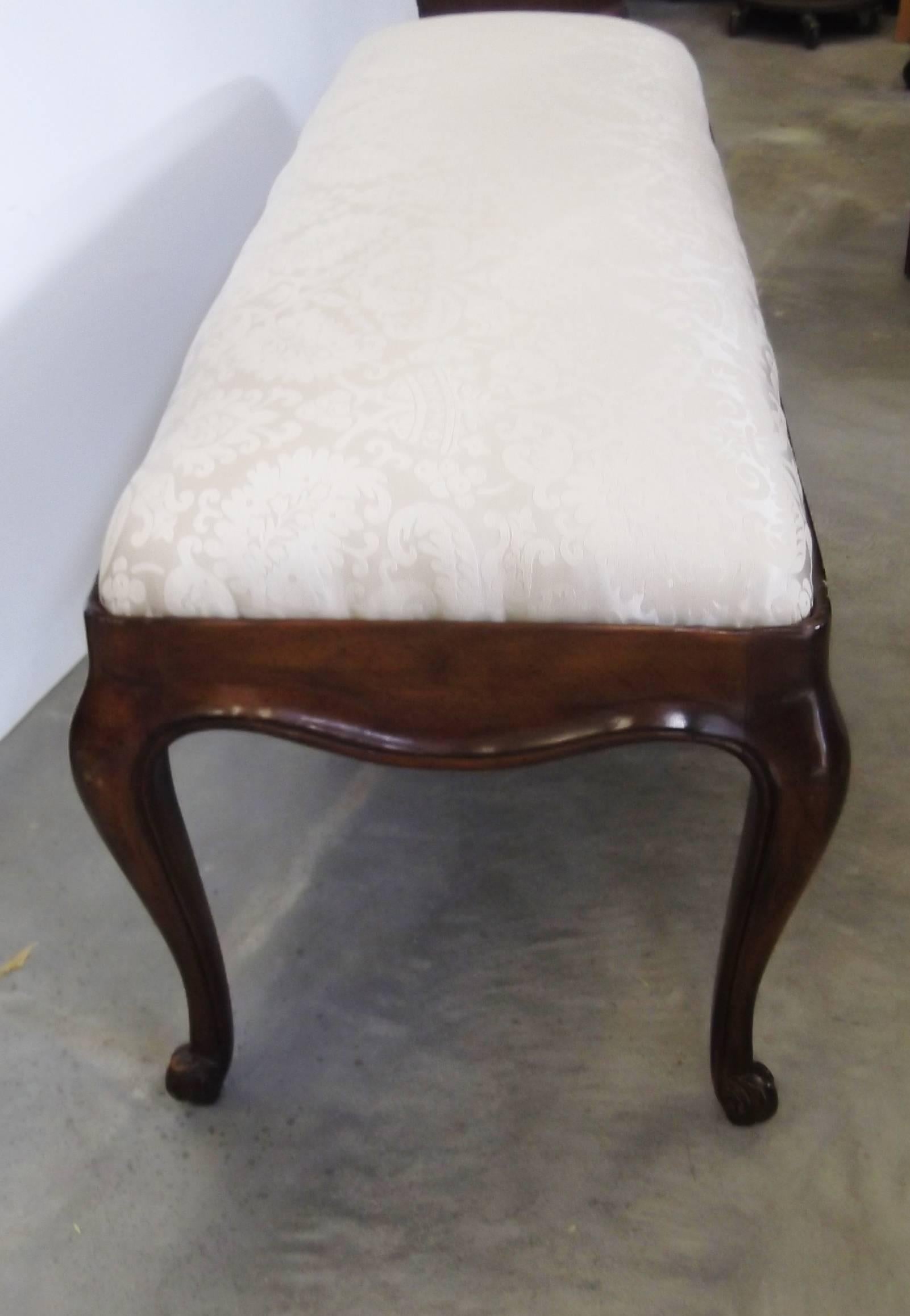 Elegant dark walnut hand-carved bench. Classic cabriole legs with scrolled feet and nice carved detail on the apron. Newly covered in a light butter colored damask.