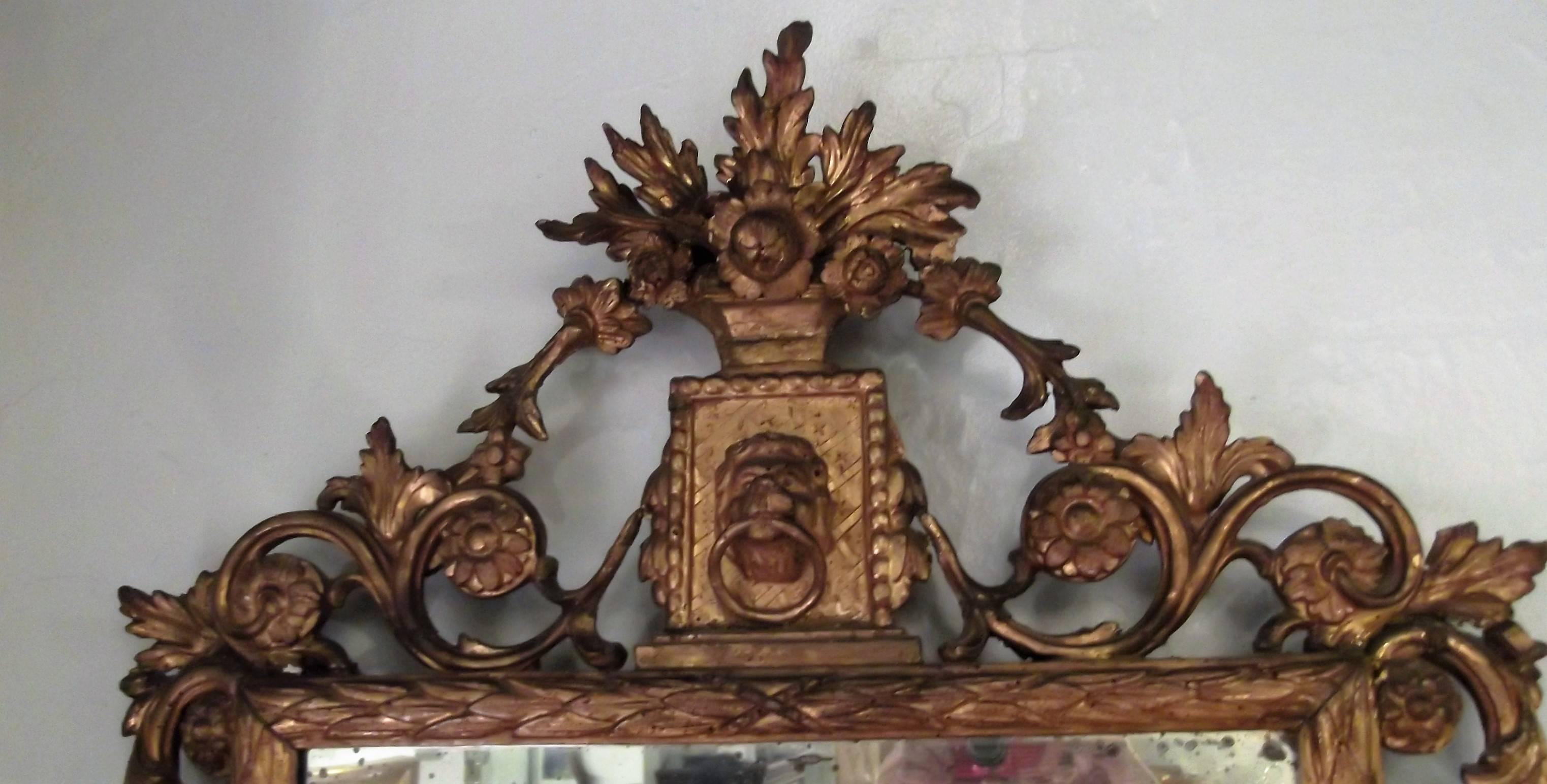 Authentic 18th century Italian mirror, the molded frame carved with laurel leaves. the tall crest with a lion mask surmounted by a basket of flowers and foliate scrolls with flower head paterae at the sides, the base with foliate scrolls and spurs.