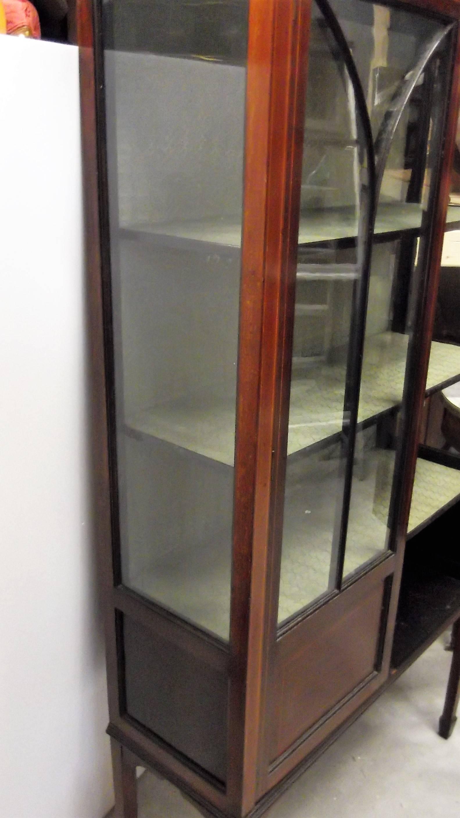 A mahogany with satinwood pencil inlay display case cabinet. The overhanging top above two individually glass pained doors resting on four tapered legs The interior has two shelves, the lower section had wood panels for closed storage. The lock