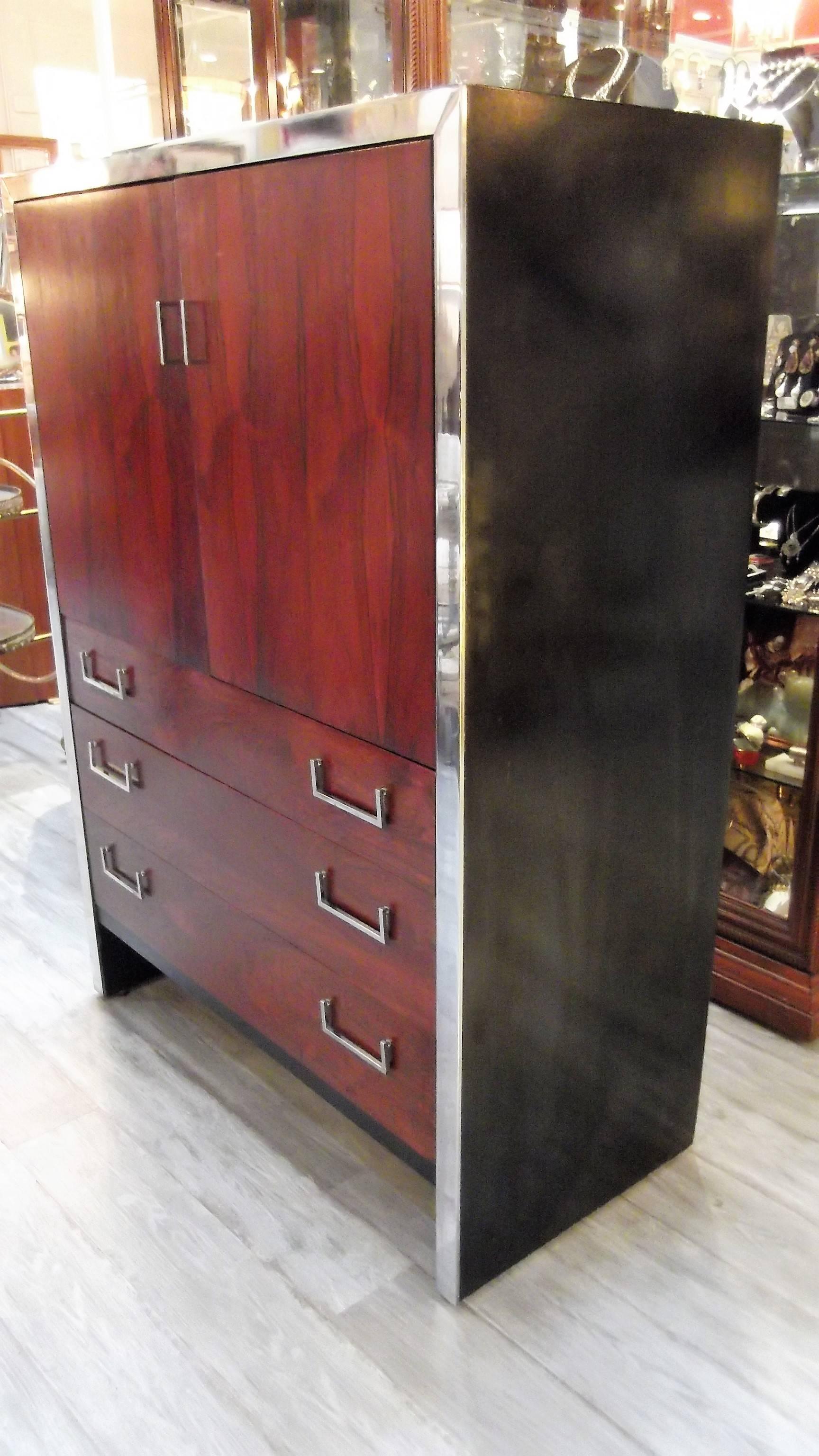 Rich rosewood grain complimented by polished chrome trim and hardware. Designed by Milo Baughman for W J Sloane with black lacquer sides, drawer and cabinet storage, sleek Mid-Century design.