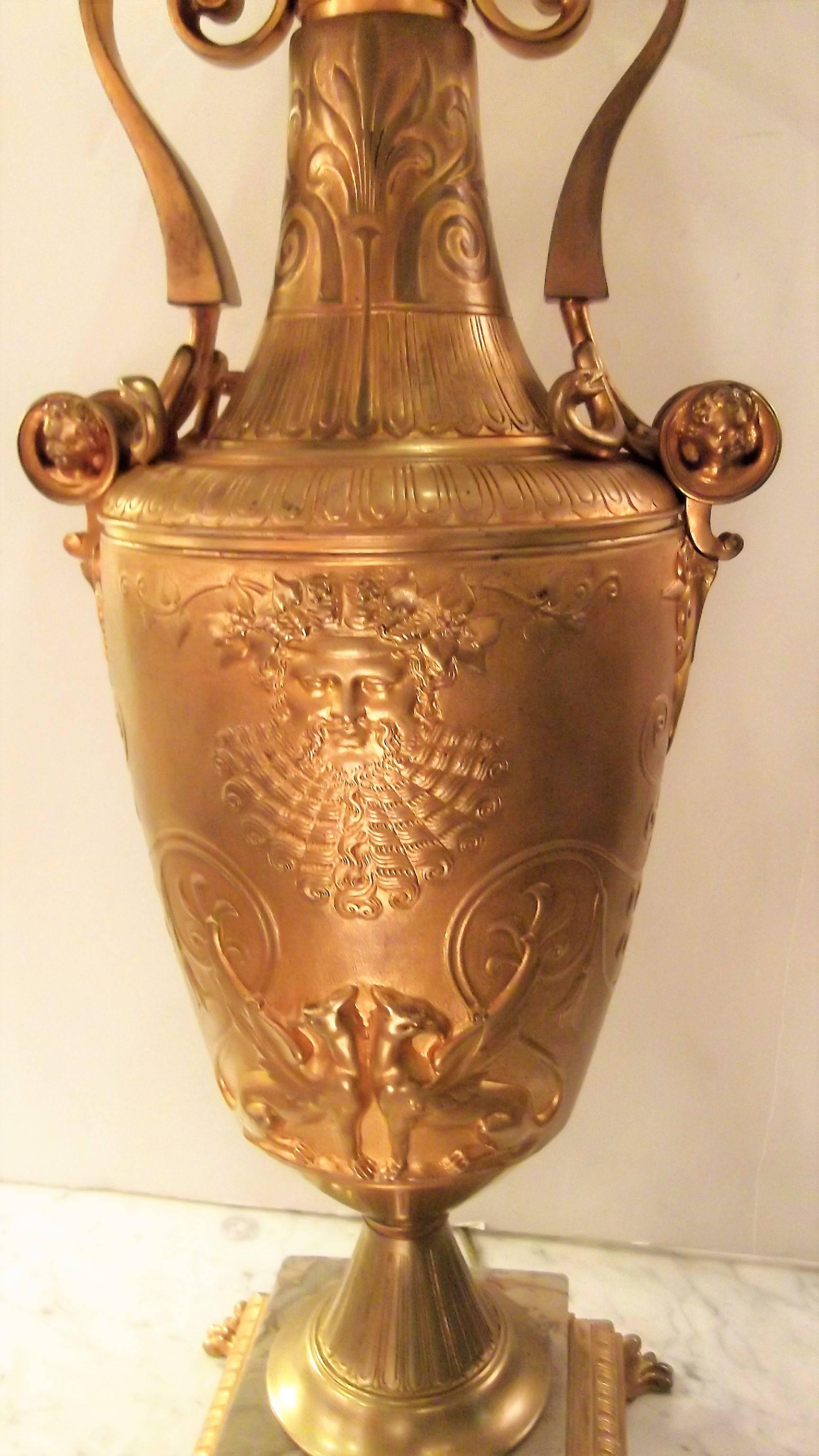 Neoclassic gilt bronze urn made in France, circa 1865. Beautifully cast bronze urn with double handles with neoclassic faces on the front and back. The handles have applied serpant decoration. The base has an inset of a neutral color marble resting