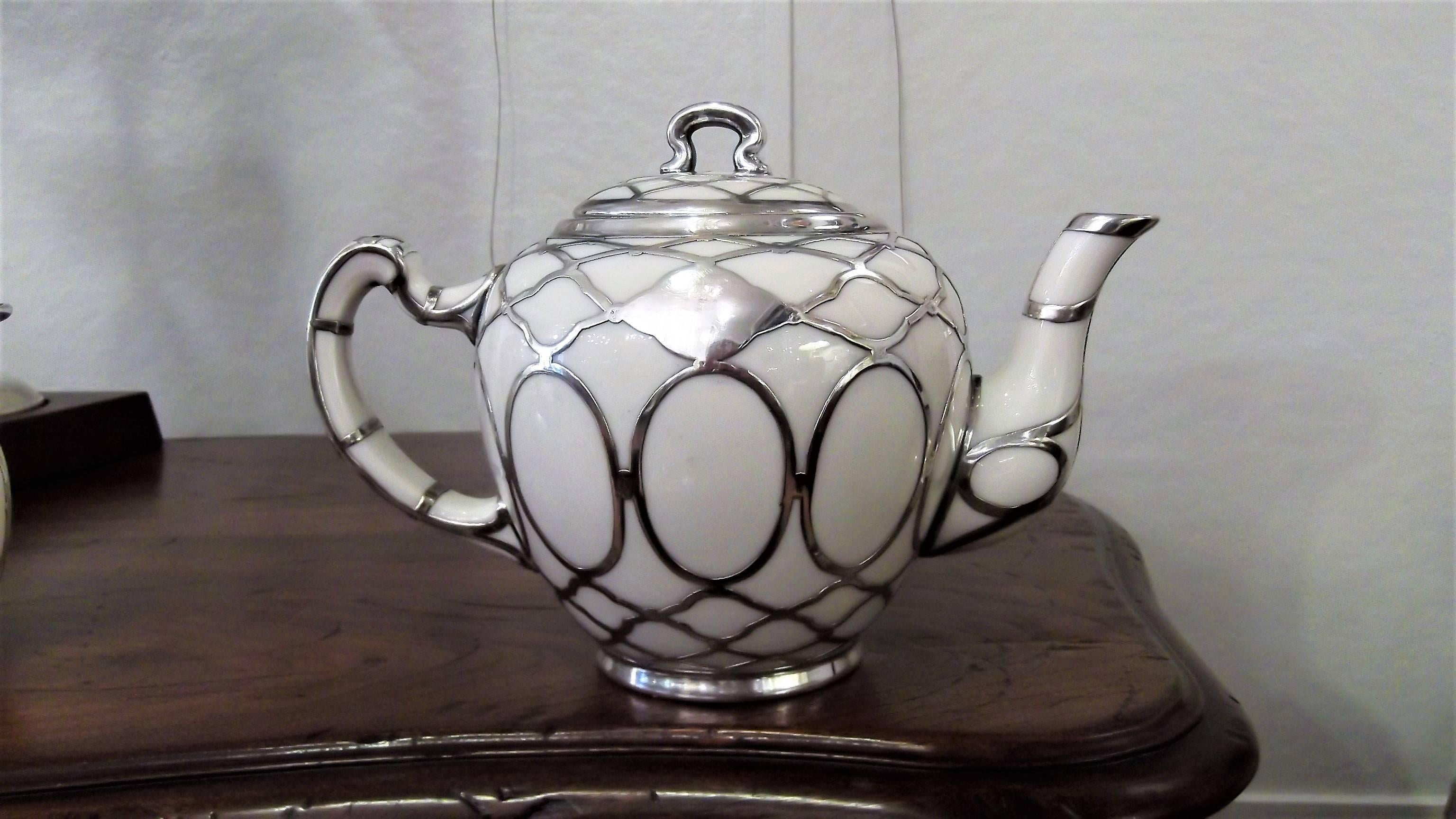 Beautiful three-piece tea set with sterling silver overlay. Early 20th century Lenox green mark on the bottom. The teapot retains its original strainer used for make tea with loose tea. Complete with its small milk jug and lidded sugar bowl.