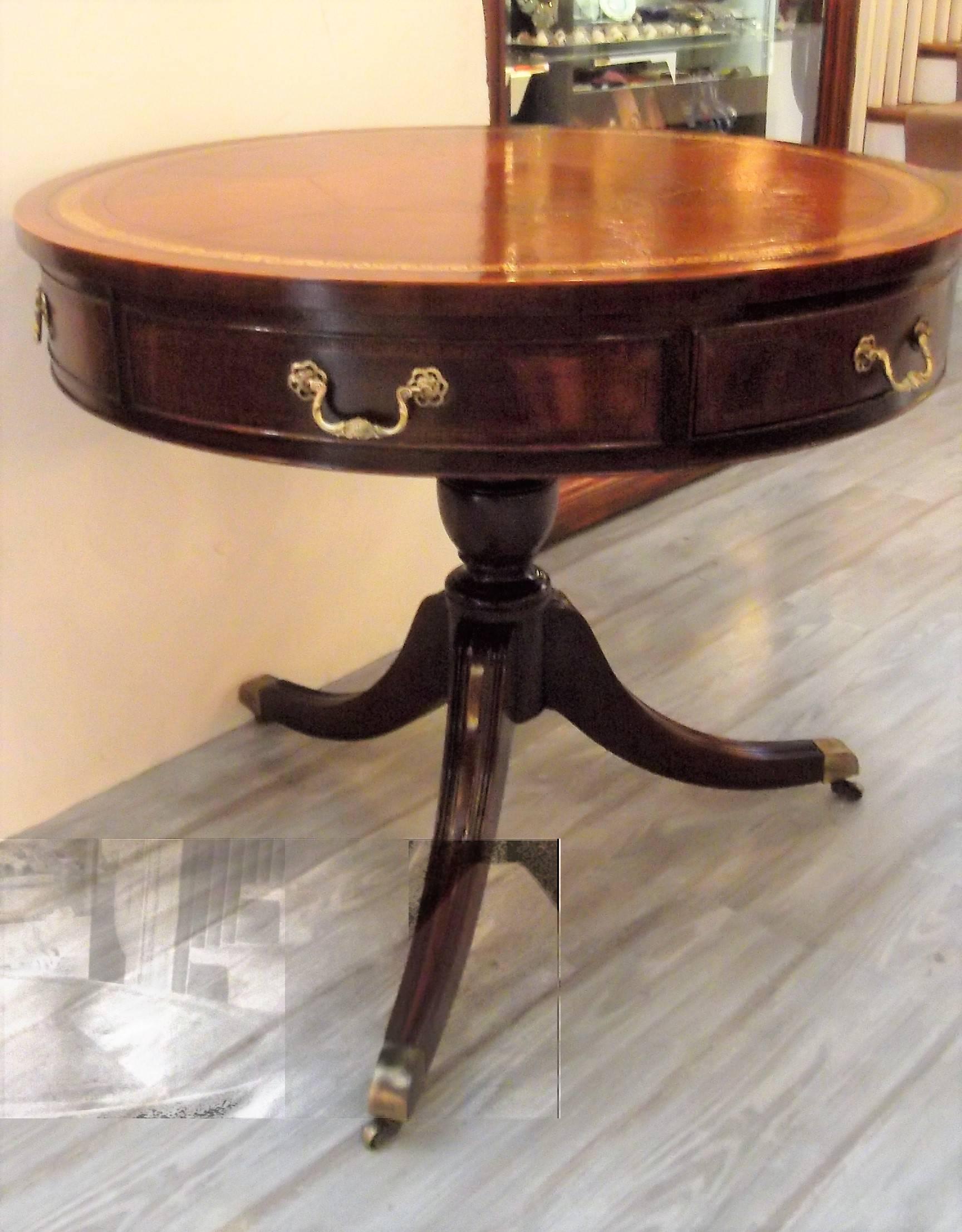 Round mahogany drum table with aged leather gilt tooled top. The apron appears to have six drawers with cast brass handles. The front and back drawers are working drawers. The top is in very good condition but does show some well cared for use and