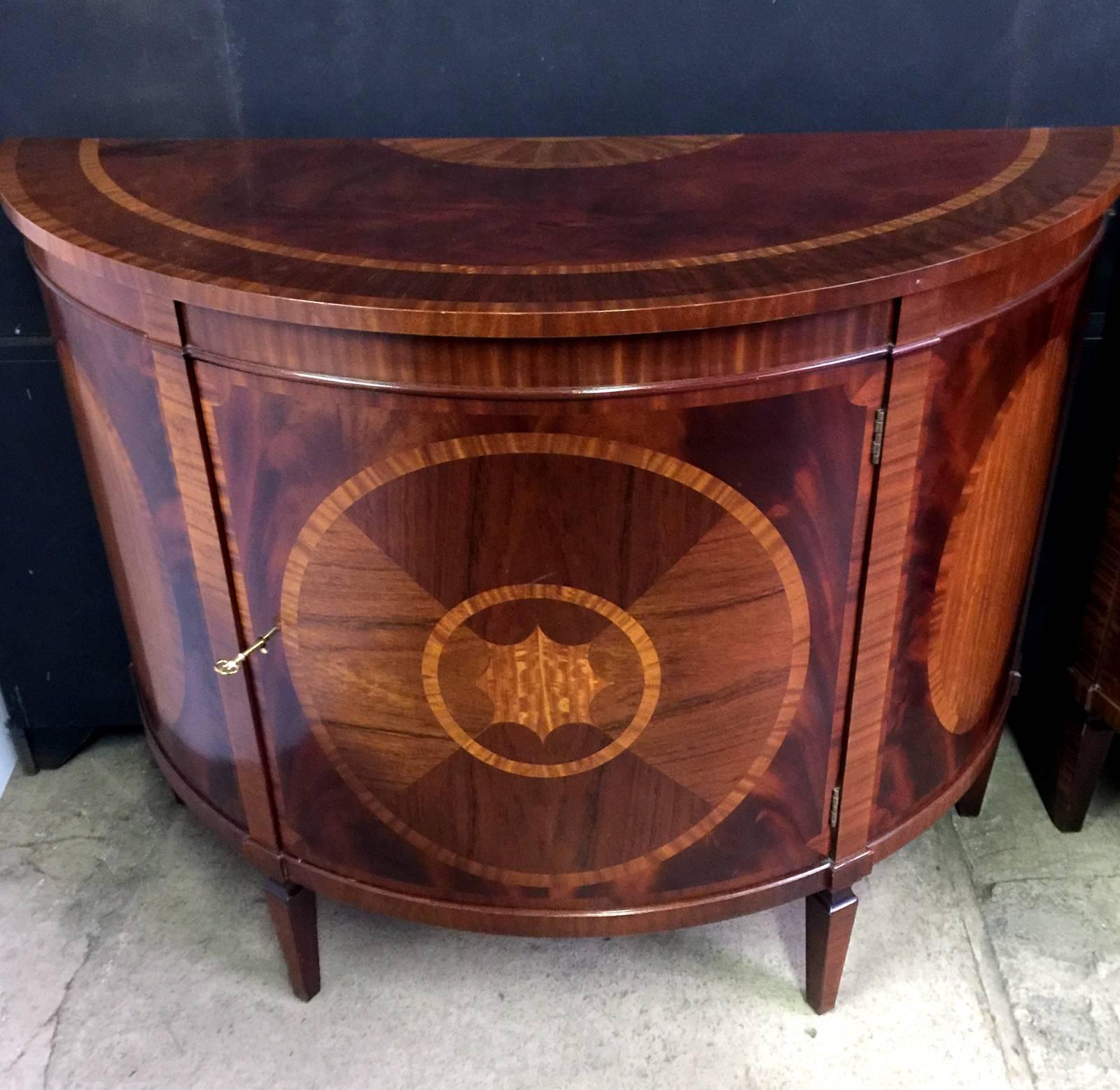 A fabulous pair of mahogany and satinwood inlaid demilune commodes. The highly inlaid tops over a curved inlaid door complete with shelf resting on four tapered feet. Made by the premier American furniture company. Baker....complete with keys.