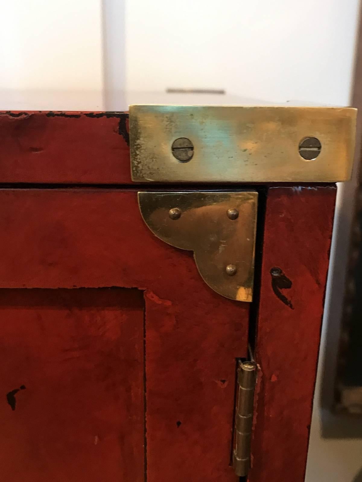 Asian style chest with three drawers next to doored storage over one larger drawer. The polished brass handles and corners are in a Campaign style. The hand-painted finish is a cinnabar color with smokey black over-painting. Made By Century.
