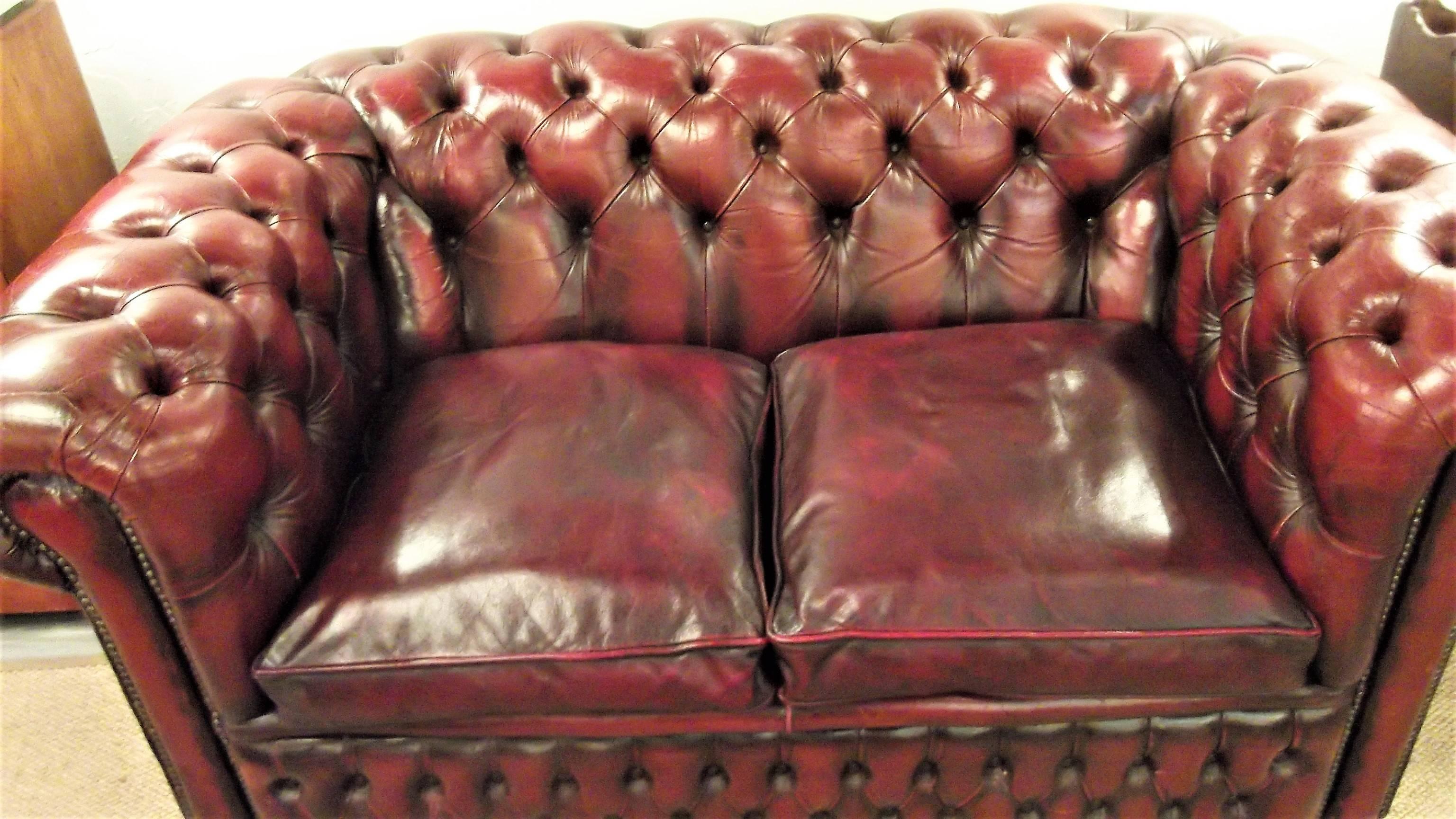 Classic English Chesterfield love seat with original cordovan leather. The arms and back have deep biscuit tufting with the seat being loose cushions.