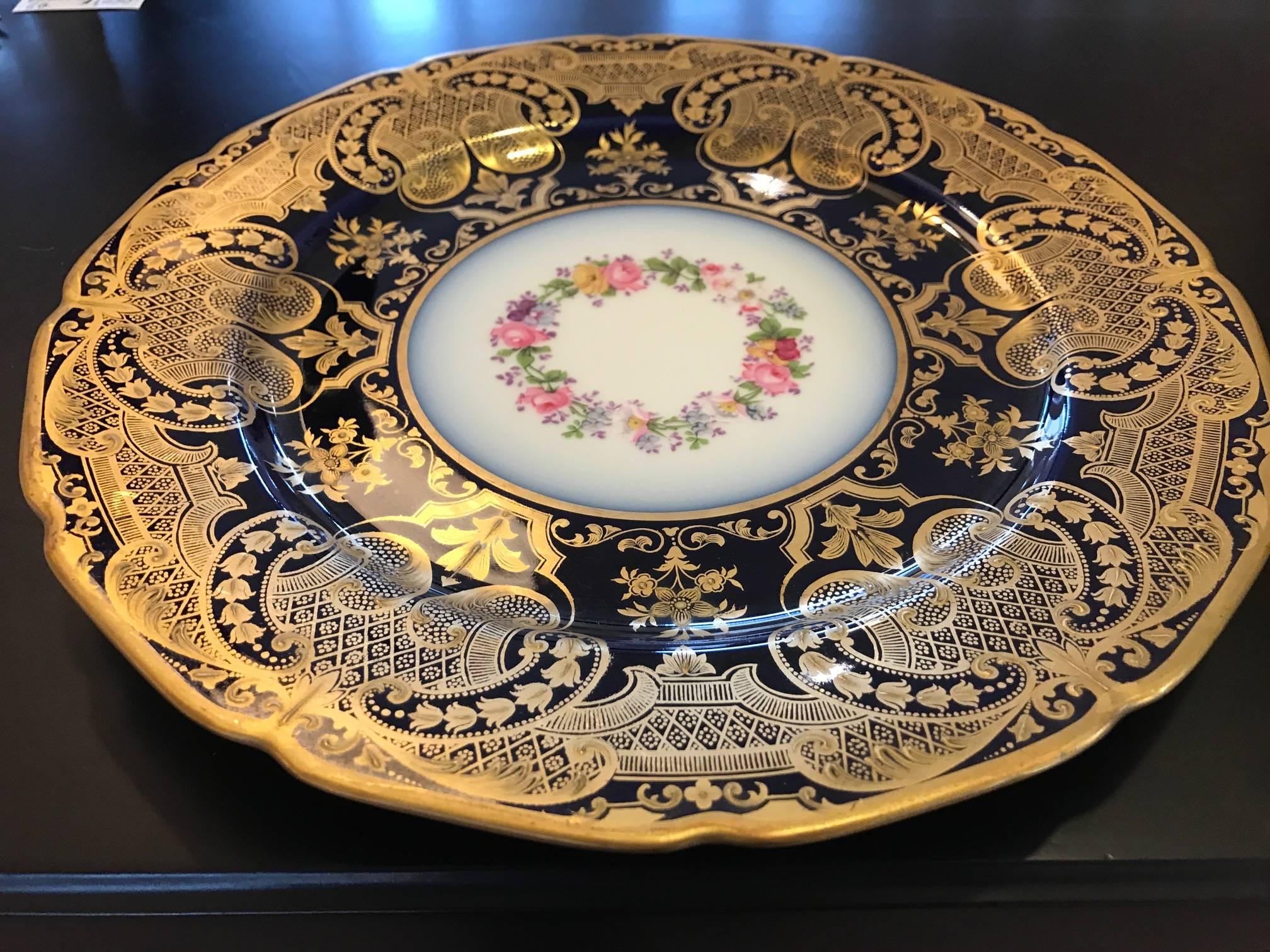 A set of 12 stunning elaborately gilt and cobalt service plates. The opulent borders with raised gilt decoration with hand-painted floral centers. Made by William Guerin Limoges France.  This set is in excellent condition and were mostly used as