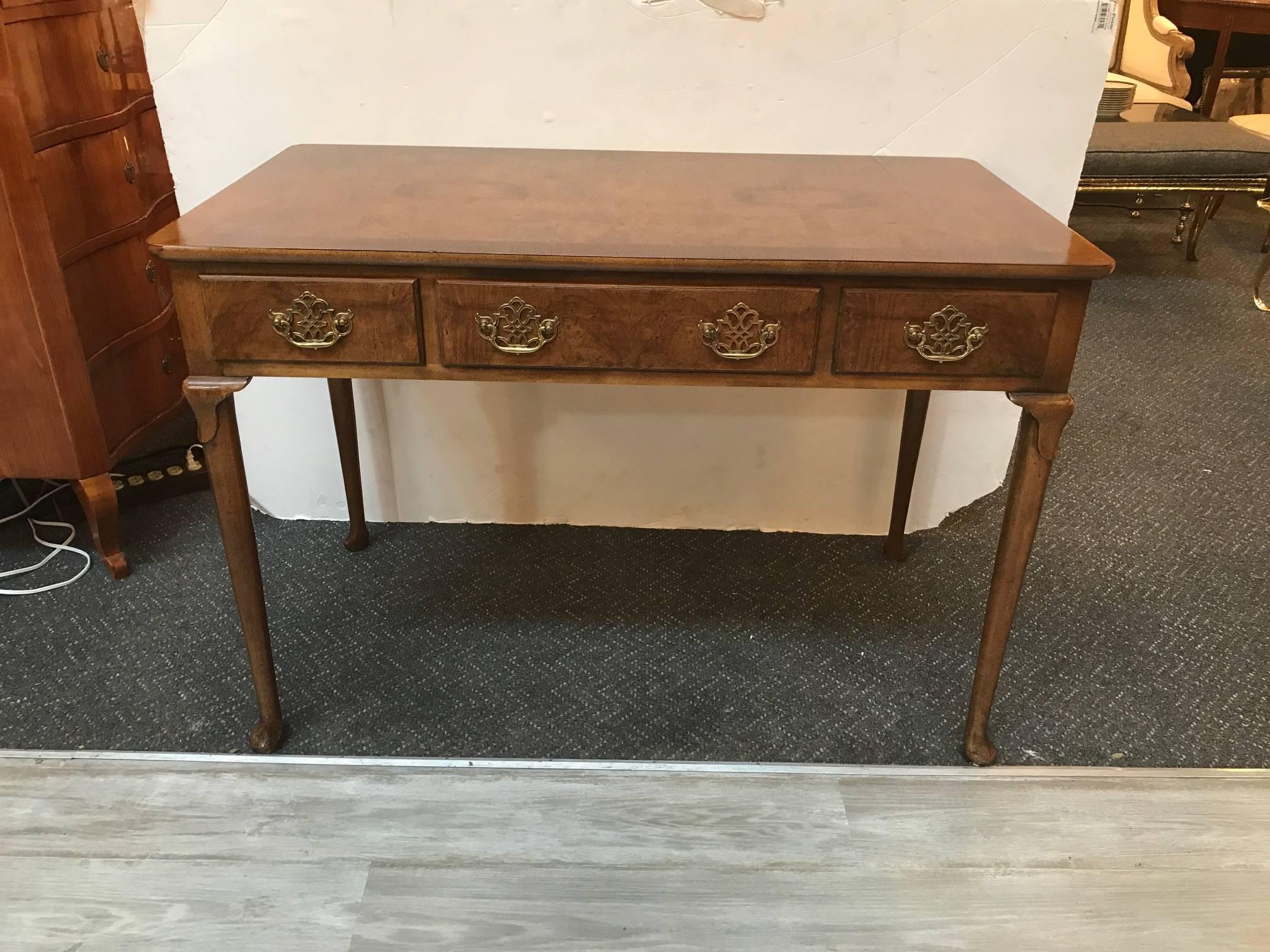 Classic English style writing table desk by Baker. The burl walnut top supported by four slightly carved Queen Anne legs with pierced Chippendale style solid brass hardware, marked baker inside one drawer. There is one centre drawer flanked by two