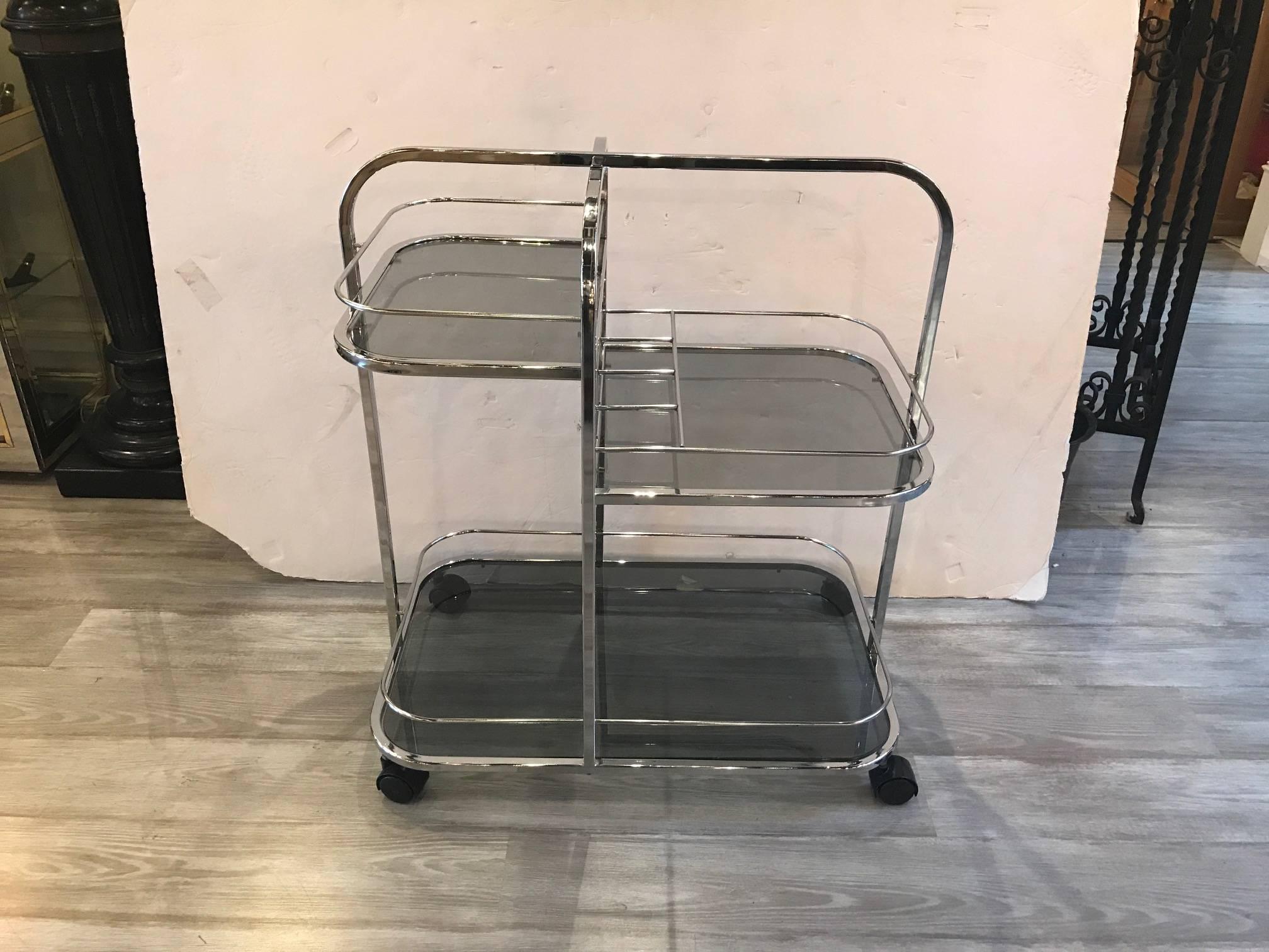 Mid-Century Modern chrome and smoked glass beverage or dessert cart. The asymmetrical upper shelf with single lower shelf in a smoked glass. The Chrome body in very good condition resting of four castors.