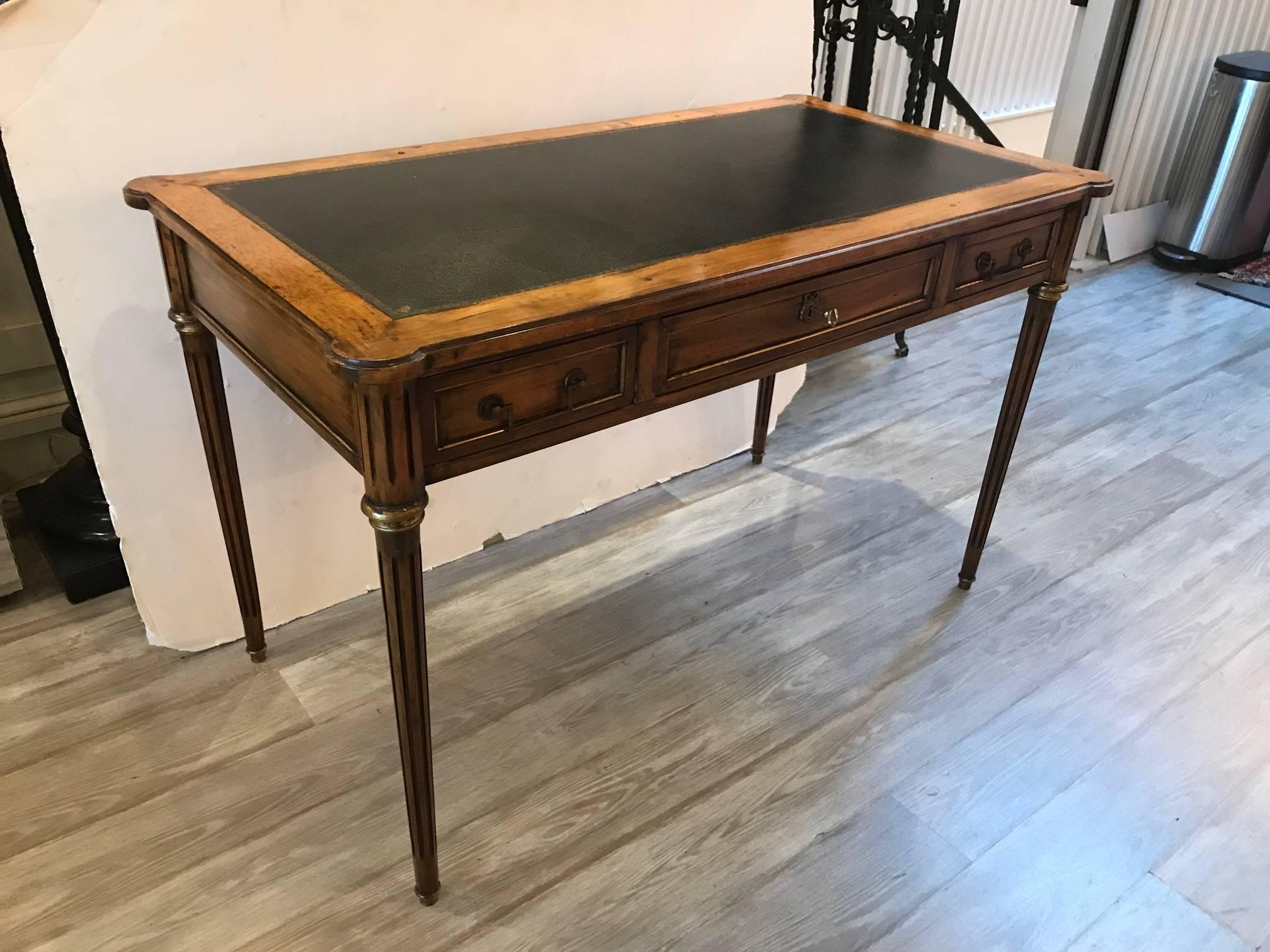 Classically styled fruitwood desk made in France. The black textured leather top with gilt tooled border with a solid fruitwood frame. The three drawers supported by four reeded tapering legs with gilt highlights. Marked on inside drawer