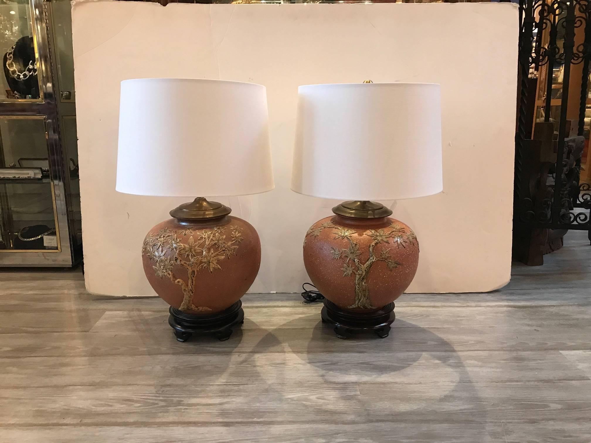 A pair of early 20th century hand thrown stoneware pots, circa 1910. The pots, with a high relief decoration of branches and leaves with a glazed finish. Each one is made and decorated. The pots have been lamped aver 50 years ago and are shown with