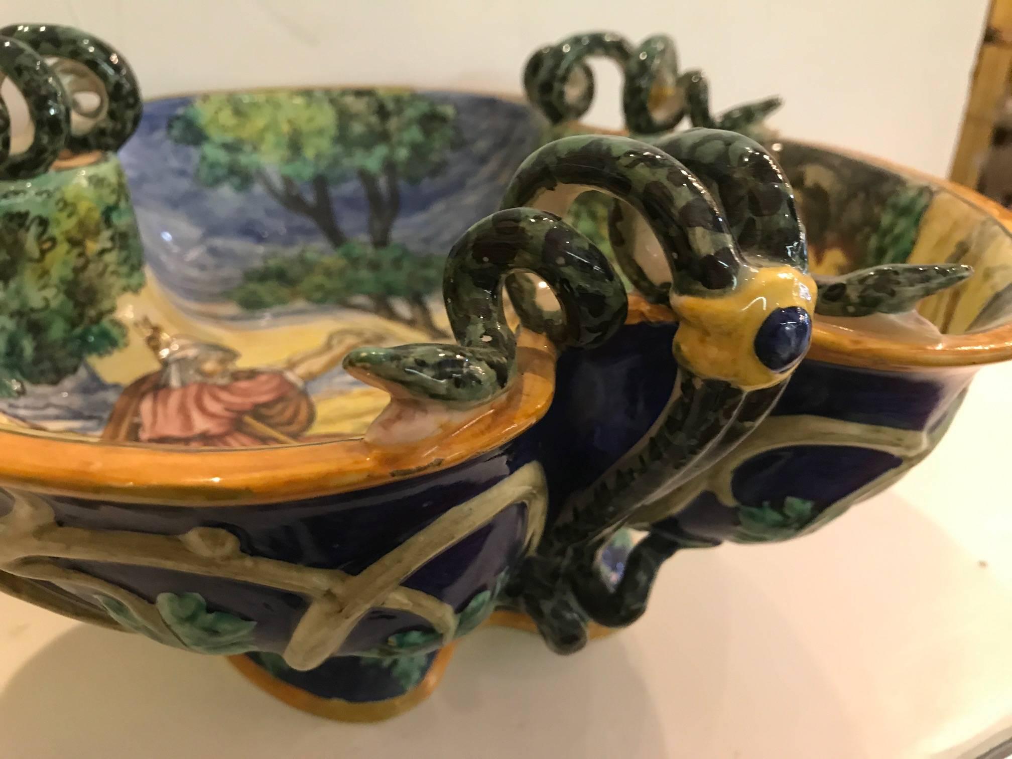 Elaborately painted Italian faience pedestal bowl. Vibrant colors with a central biblical scene with three snake handles on the outer edge. The underside with a cobalt blue background with a grape leaf pattern.